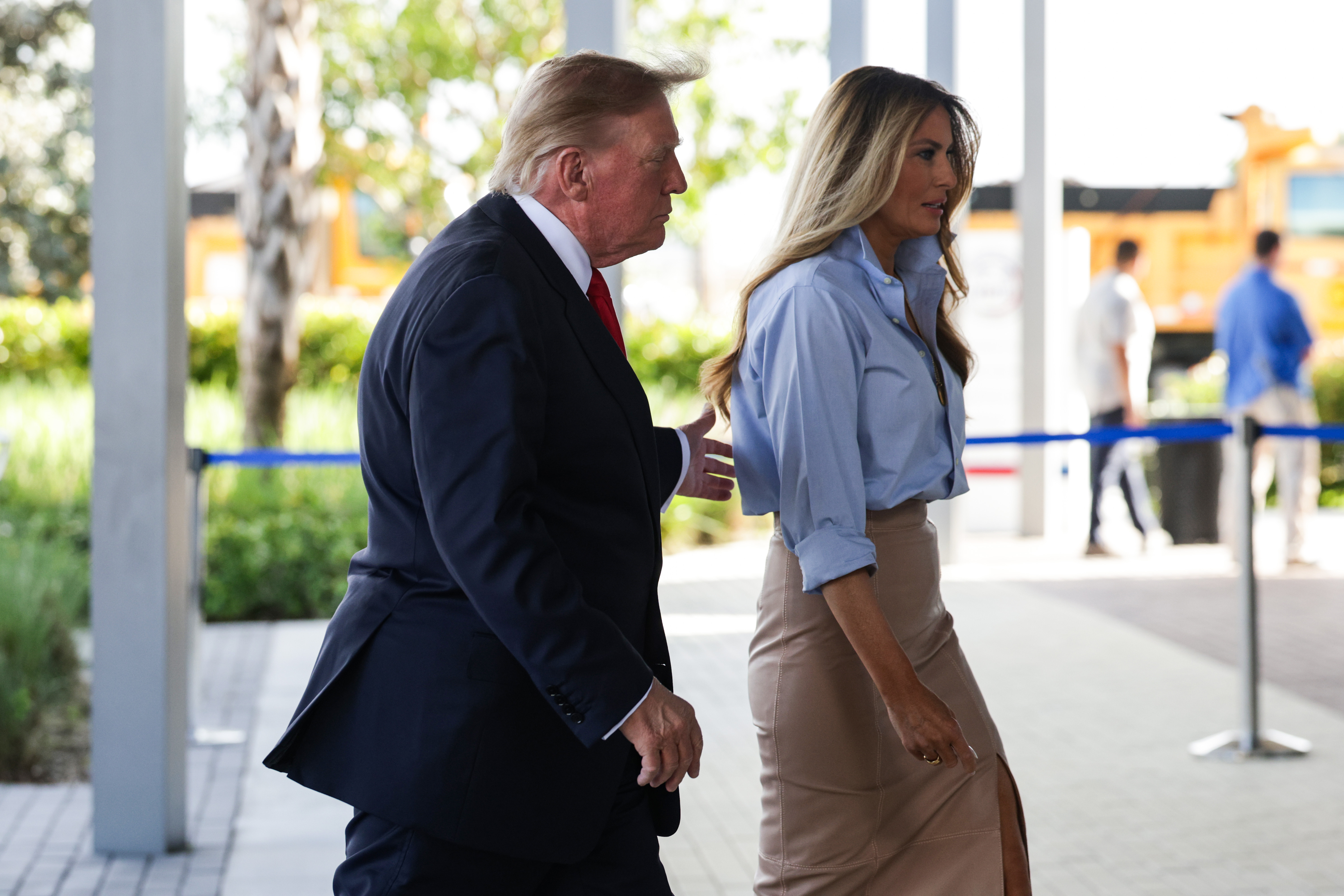 First Lady Melania Trump walks alongside President Donald Trump outside the Palm Beach County Supervisor of Elections office in West Palm Beach, Florida, on October 24, 2026, to cast early ballots in the midterm elections. Bringing effortless structure to daytime dressing, she pairs an unbuttoned sky-blue shirt and high-waisted beige slit pencil skirt with soaring nude pointed-toe stiletto pumps that crisply elongate her stride.