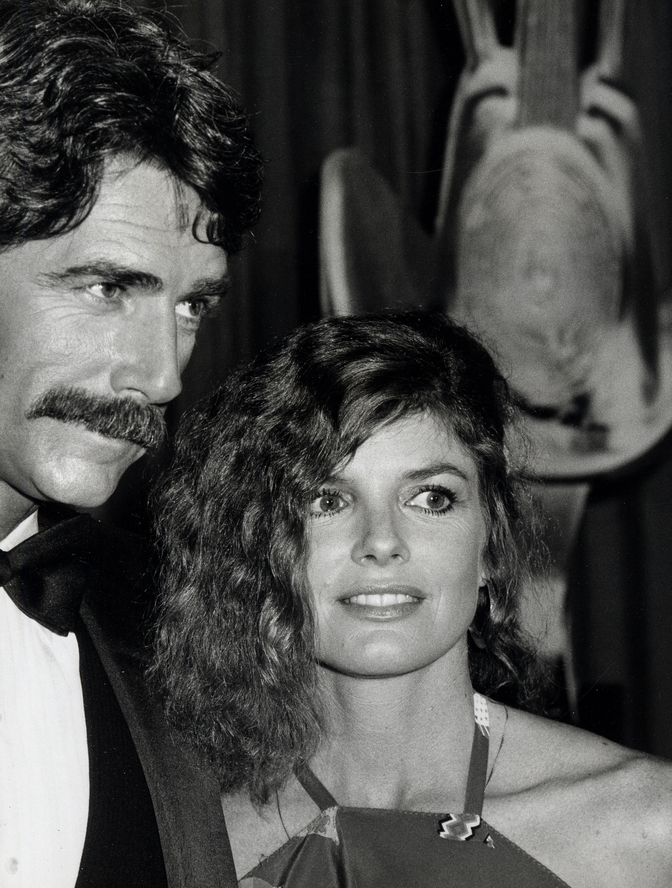 Hollywood couple Sam Elliott and Katharine Ross turned heads at the 16th Annual Academy of Country Music Awards held at the Shrine Auditorium on April 30, 1981. Sam exuded classic charm in a black tuxedo with a matching bow tie and his signature thick, dark mustache, while Katharine smiled brightly at his side, showcasing voluminous, shoulder-length brunette waves and an elegant halter-neck evening dress. | Source: Getty Images