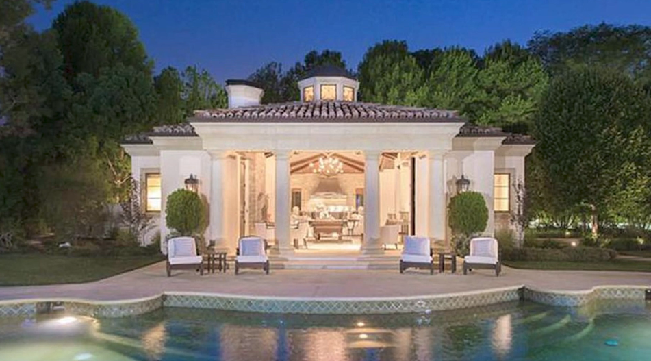 The open-air poolside cabana features a tiled hip roof topped by an architectural cupola, flanked by manicured topiaries, sun loungers, and classical columns directly overlooking the pool edge. | Source: YouTube/Taste of Country