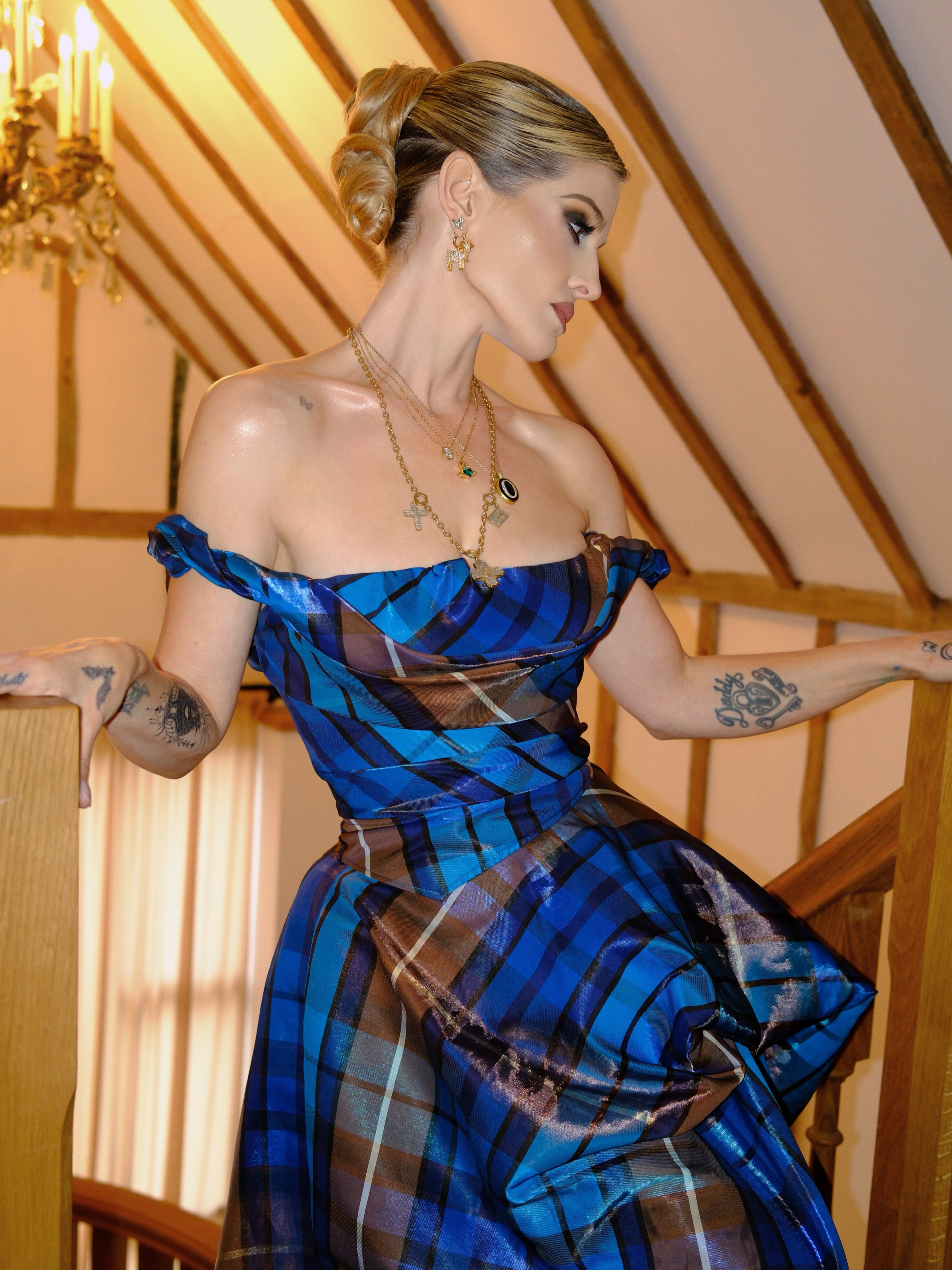 Striking a dramatic pose on a wooden staircase, Kelly showcases the asymmetrical silhouette and voluminous skirt of her €3,485 Vivienne Westwood tartan gown, letting the fabric do all the talking. | Source: Instagram/kellyosbourne
