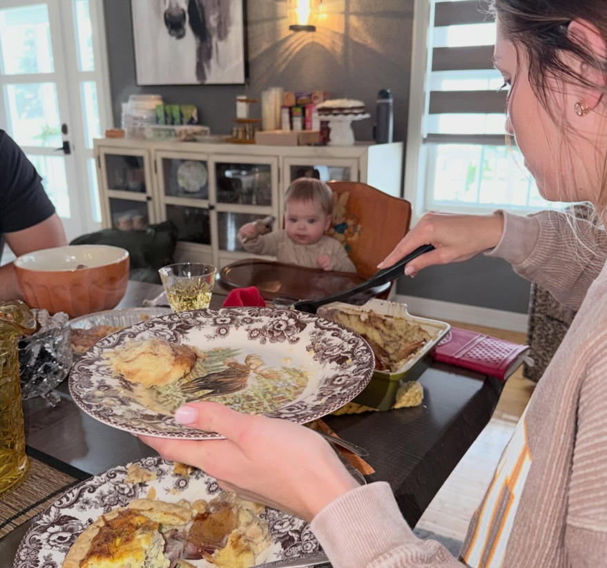 A family meal shows the same table in use, with serving dishes, patterned plates, and glasses spread across it. A glass-front cabinet and a child's high chair are also visible nearby. | Source: Facebook/kristi.noem