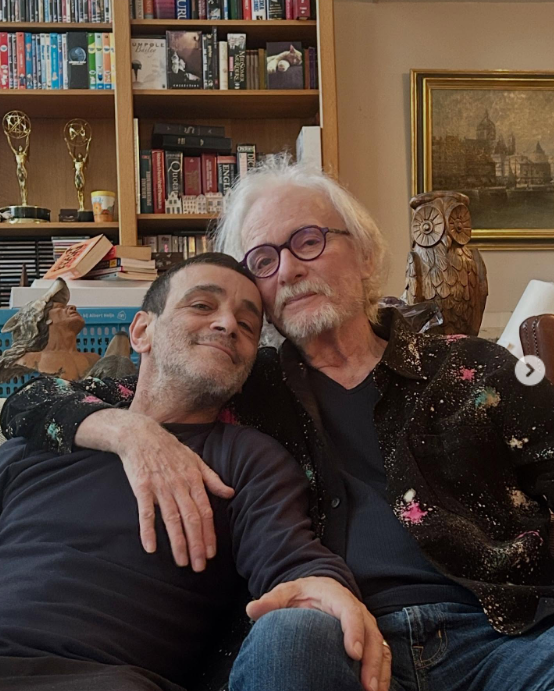 Anthony Geary and his husband Claudio Gama sitting on a sofa in their home in Amsterdam, from a post dated December 5, 2025 | Source: Instagram/claudiogama_71