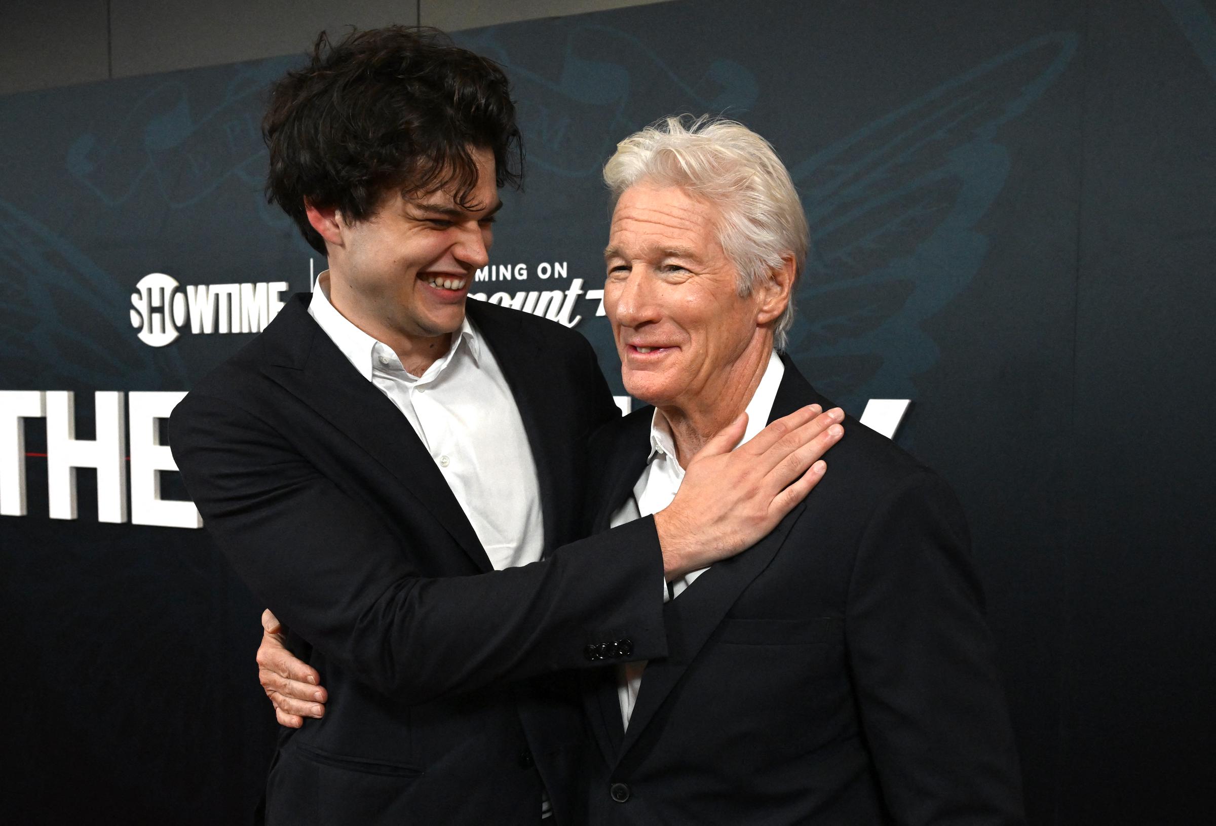 Homer Gere wraps an arm around his dad, Richard Gere, sharing a genuine laugh at "The Agency" premiere in New York City. The father-son duo radiates warmth and charisma on the red carpet.