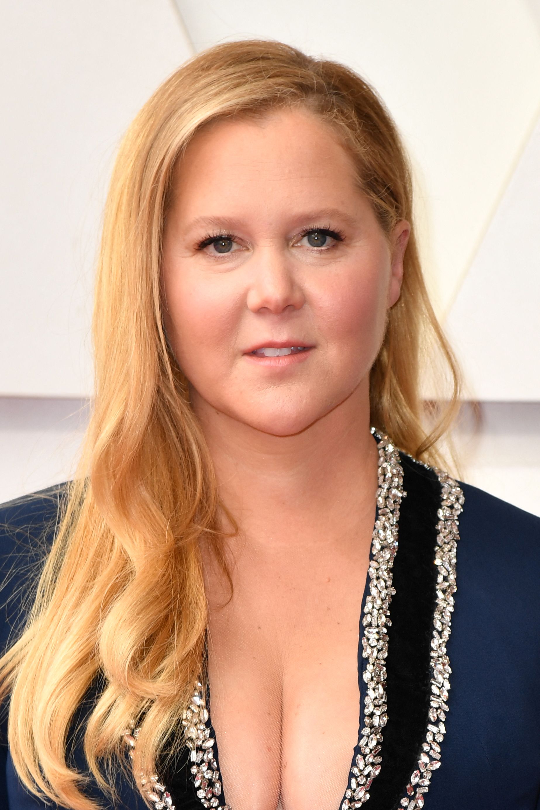 Amy Schumer attends the 94th Oscars at the Dolby Theatre in Hollywood, California. She wears a deep navy gown with silver trim and her hair styled in soft waves over one shoulder.