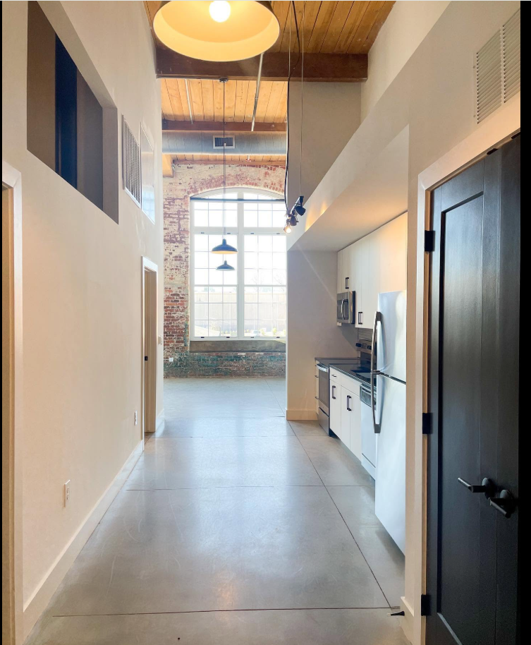 A long sightline through the loft connects the kitchen to the open living area, with exposed wood beams and a tall arched window drawing attention to the property's distinctive architecture.