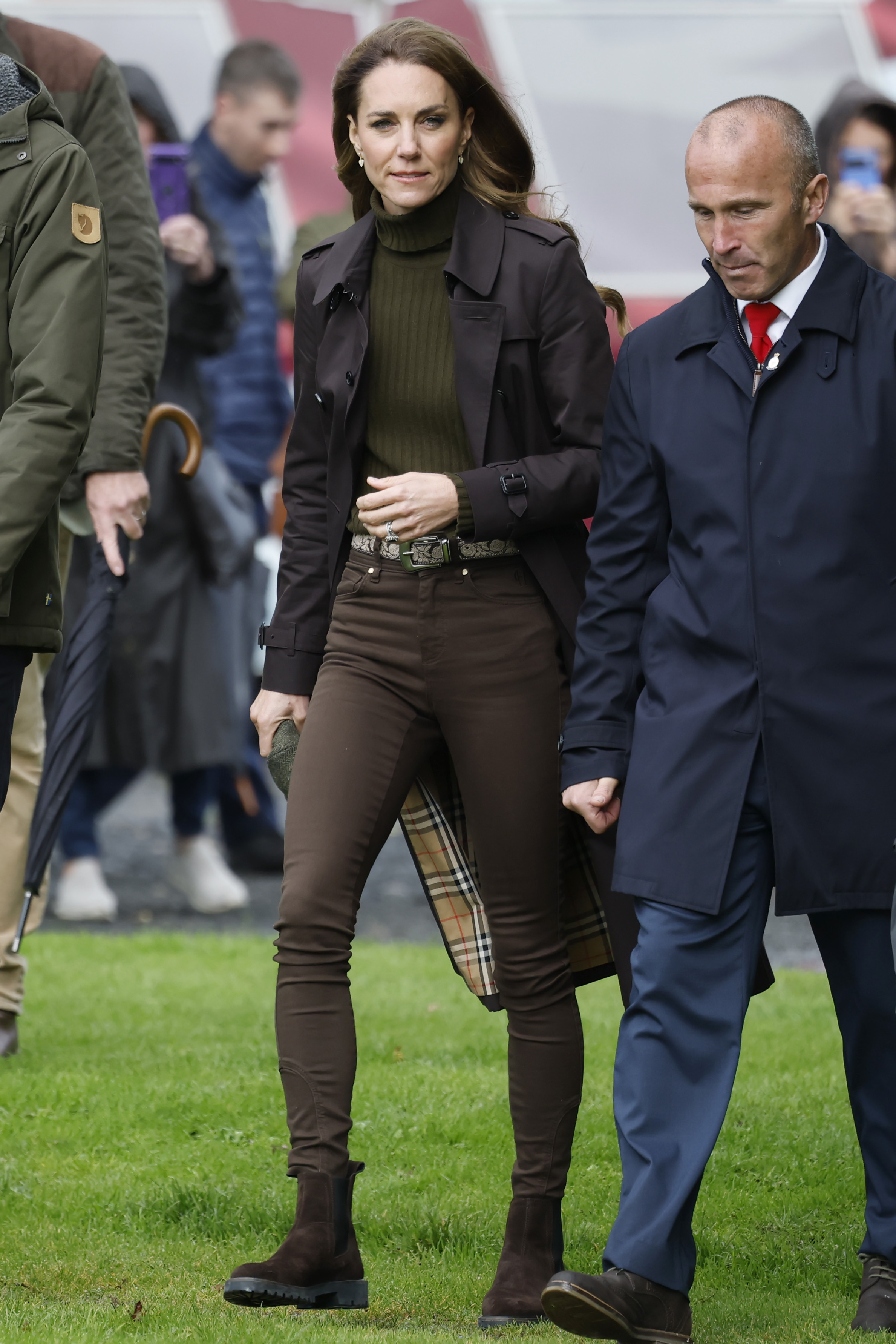Catherine, Princess of Wales, heads toward the shinty pitch alongside a club member, with her dark coat, olive green sweater, and brown trousers giving the outdoor look a polished yet practical feel. | Source: Getty Images