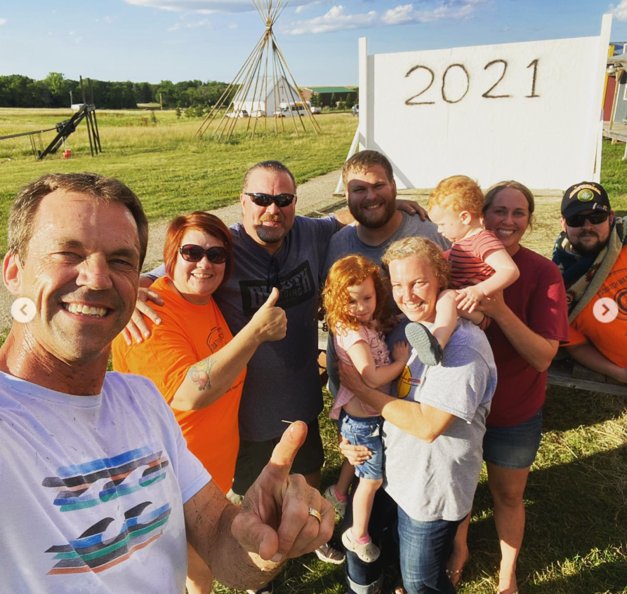 Bryon Noem beams in a group selfie, giving a thumbs-up as he stands among smiling locals—an easy, sunlit moment of community, connection, and shared pride. | Source: Instagram/sdbryonnoem