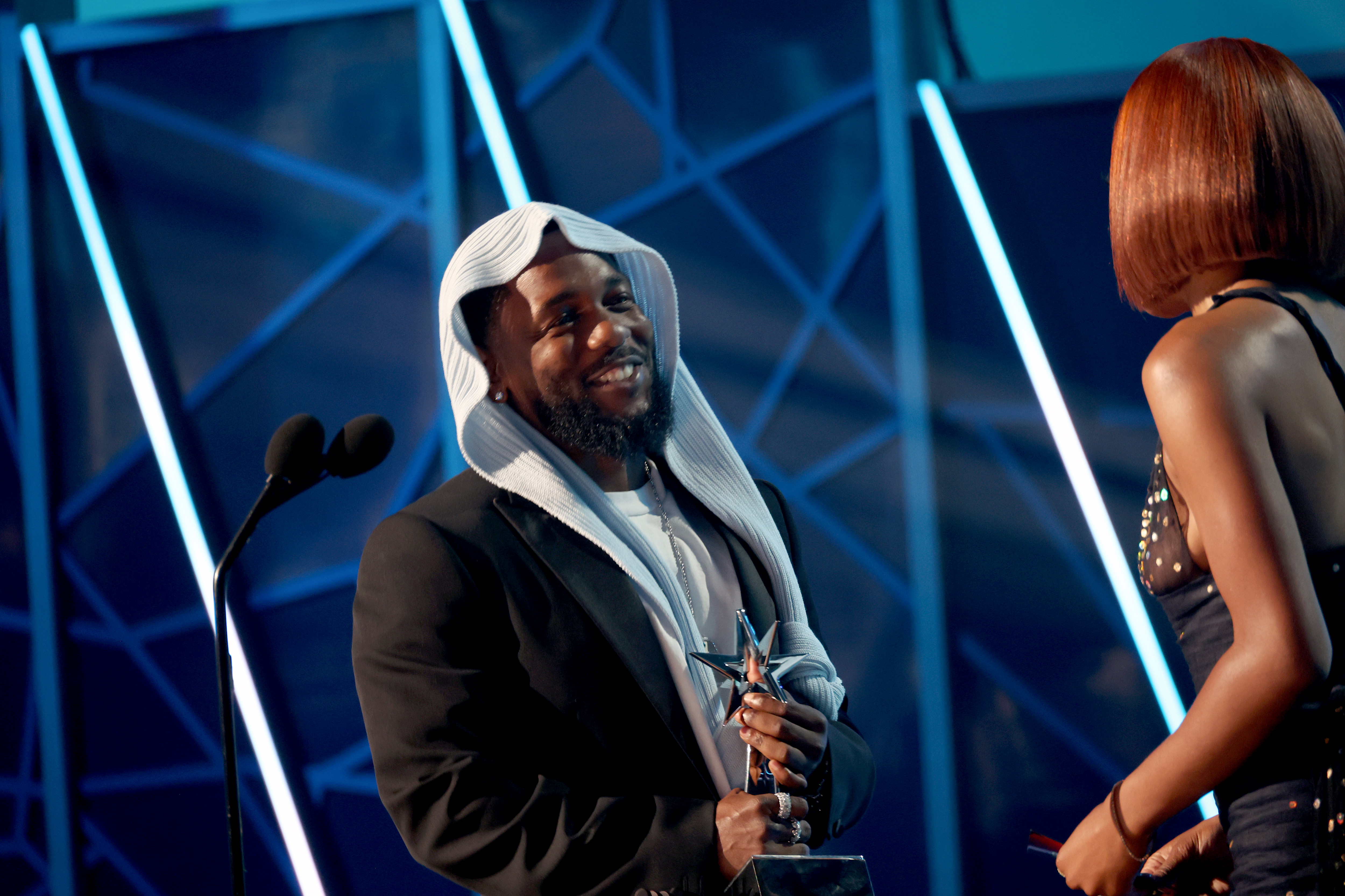 Beaming as he accepts an award, Kendrick Lamar shares a cheerful exchange with Keke Palmer during the 2025 BET Awards. The rapper's unique headwear and multiple wins made him one of the night's most talked-about stars.