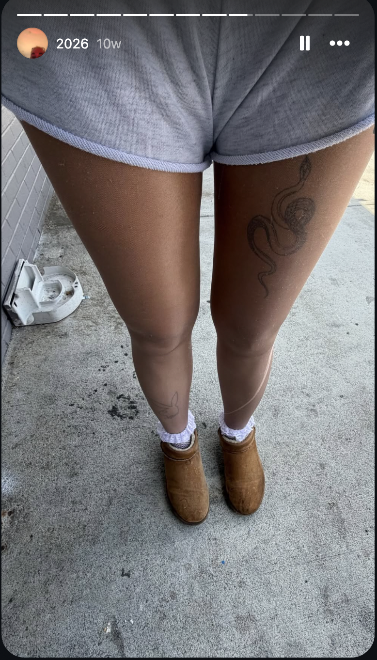 Amanda Bynes shared a close-up photo highlighting her leg tattoos, including a large snake design on one thigh and a small bunny outline near one ankle, while wearing gray shorts, white socks, and tan slip-on boots.