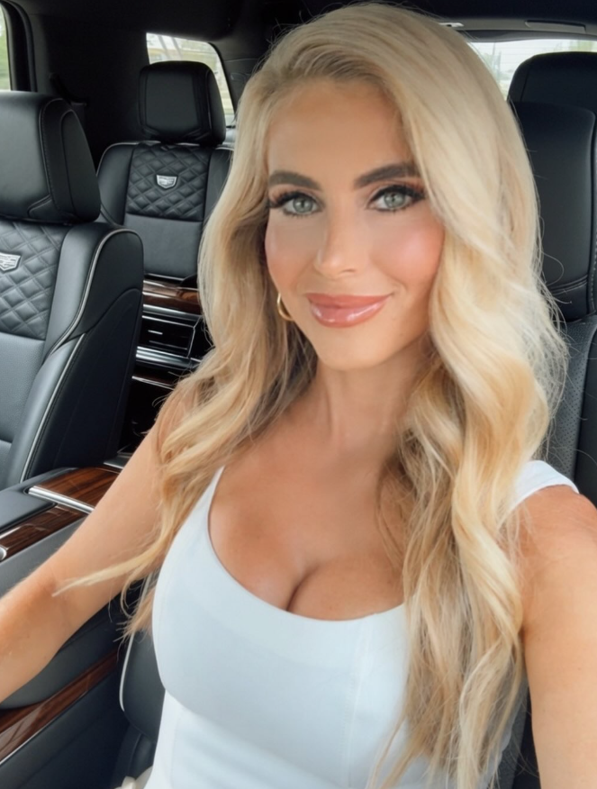 Katie Zacharia poses for a selfie in a white sleeveless top inside a luxury vehicle, with her long blonde hair styled in loose waves. Before her White House appointment, she worked in television commentary and held communications and legal roles, including a position at the Department of Homeland Security. | Source: Instagram/katiezacharia