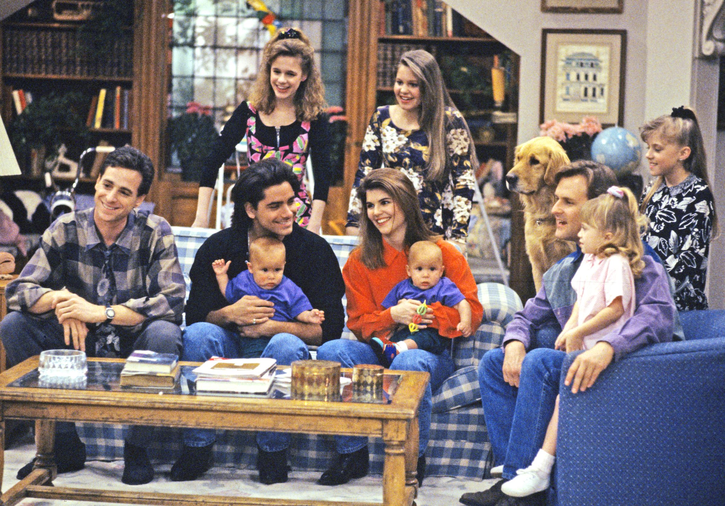 John Stamos and Lori Loughlin cradle infant twins Nicky and Alex on the living room sofa while Candace Cameron Bure and Jodie Sweetin look on alongside the rest of the household in the Season 5 episode "Captain Video, Part Two," which aired on May 12, 1992. As Uncle Jesse gathered everyone to watch his music video debut on MTV, the scene captures the warmth of the expanding family circle, highlighting how Loughlin, Stamos, and the growing sisters anchored the heartfelt humor of "Full House".