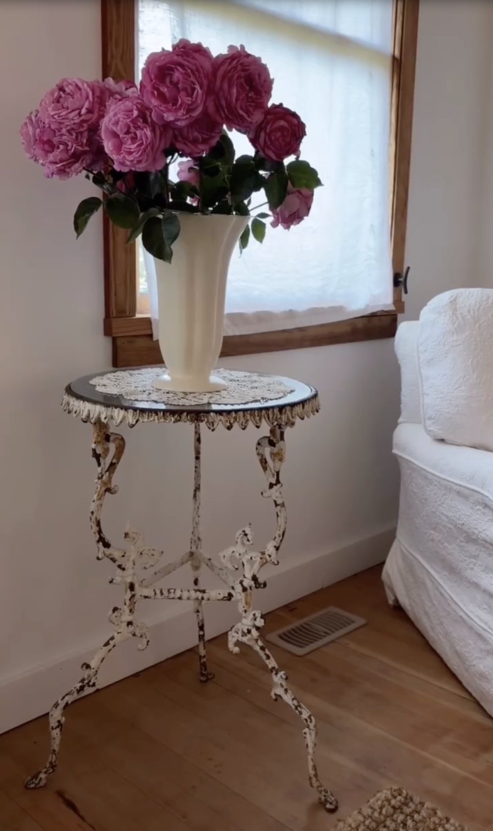 A lush bouquet of freshly cut pink Yves Piaget roses sits in a fluted cream ceramic vase, perched on an ornate, weathered cast-iron table by a sunlit window at Arcady. Showcasing the romantic charm of Pamela Anderson's Vancouver Island home, the blooming arrangement brings her bountiful garden indoors with classic cottage elegance. | Source: Instagram/pamelaanderson