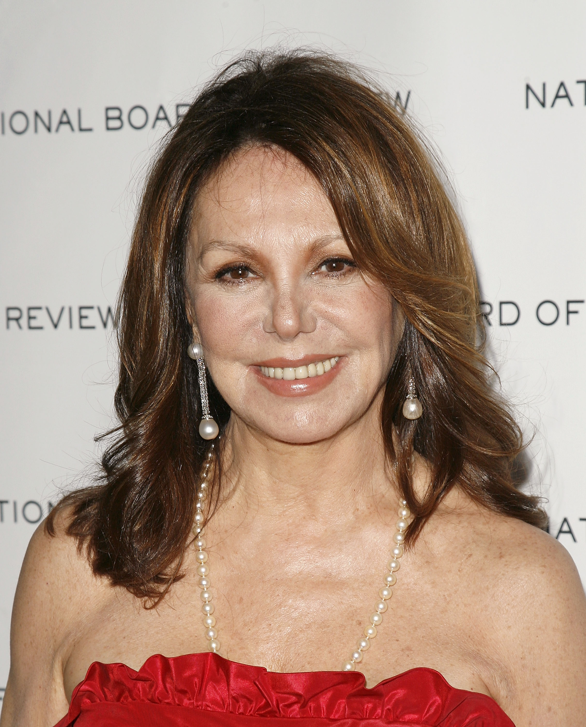 Marlo Thomas poses on the arrivals carpet at the National Board of Review Awards Gala, pairing a red strapless gown with pearl jewelry and soft waves. | Source: Getty Images