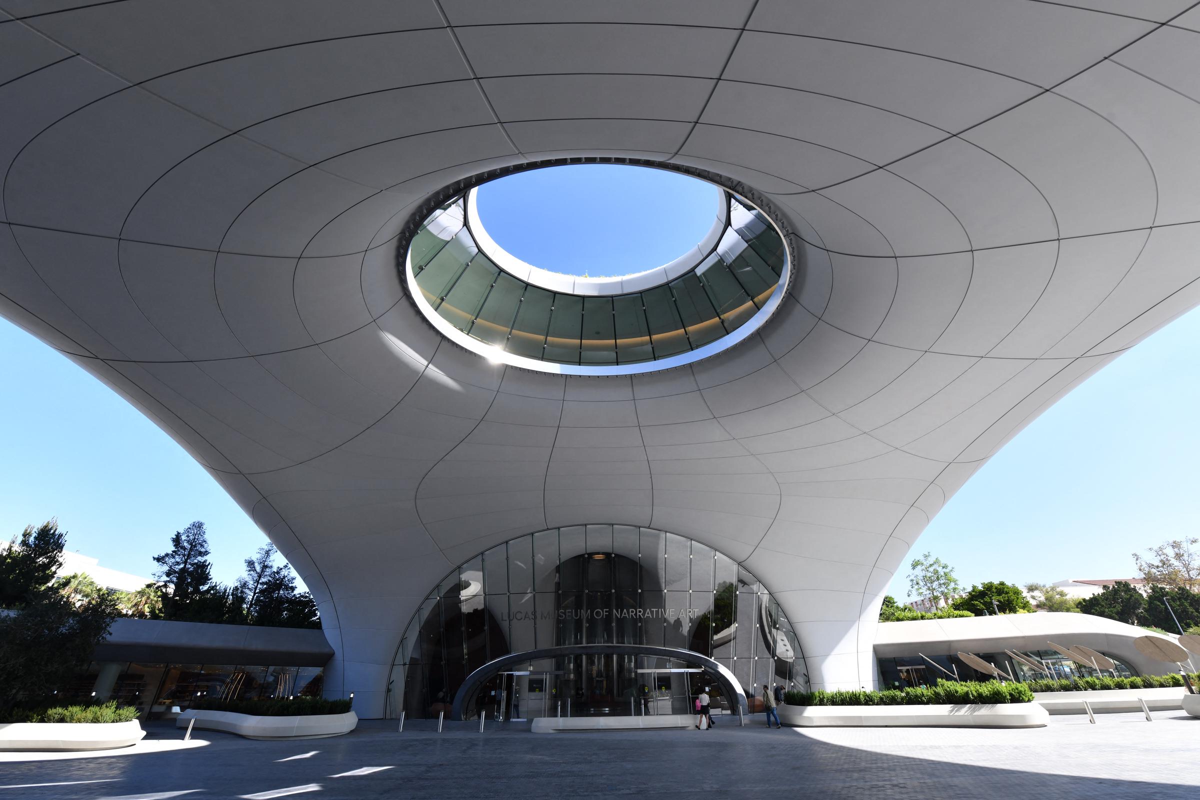 The museum's main entrance sits beneath the building's curved exterior and large opening to the sky. The view highlights how the architecture creates a sheltered public space beneath the structure. | Source: Getty Images