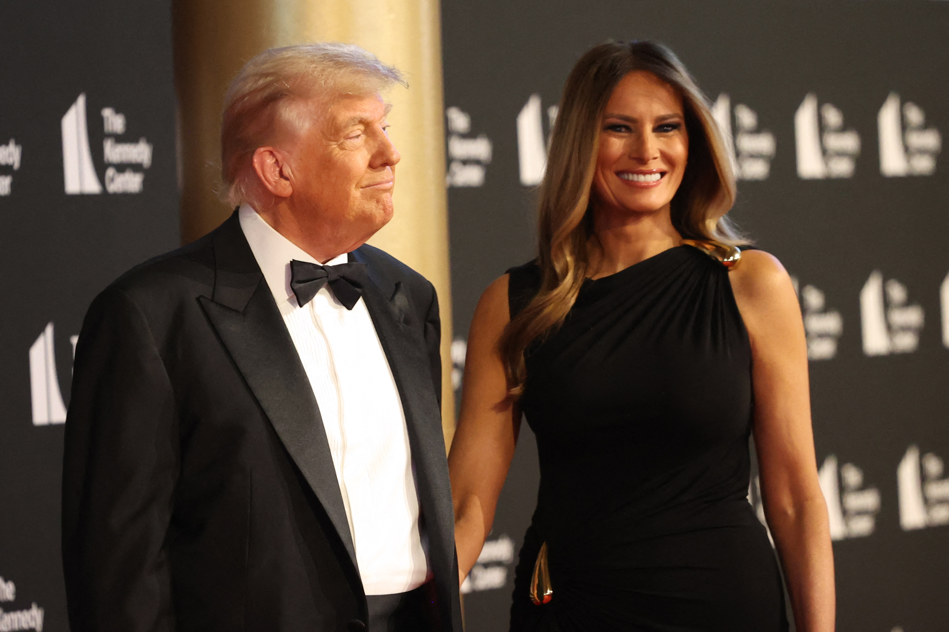 The president looks toward the first lady as she beams with a bright smile, the couple sharing a rare lighthearted exchange on the red carpet at the Kennedy Center.