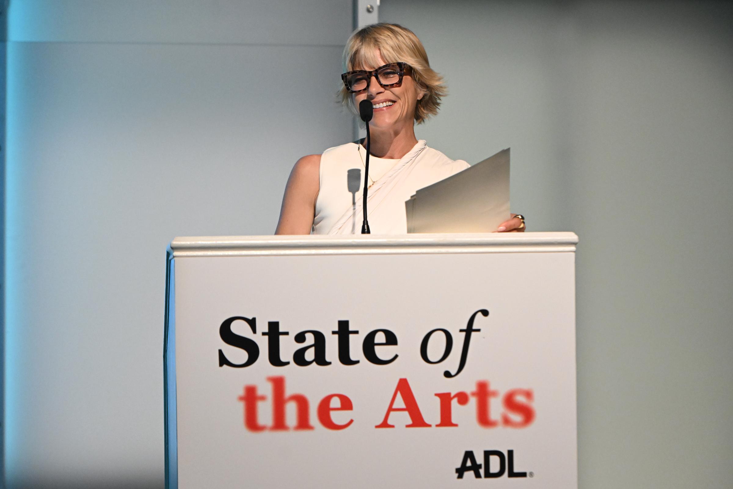 Selma Blair smiles warmly while speaking at the podium during the ADL State of the Arts: An Evening at The Jewish Museum on October 1, 2026, in New York City. She wears a sleeveless ivory high-neck top paired with tortoiseshell statement eyeglasses, holding her notes as she addresses the audience. | Source: Getty Images