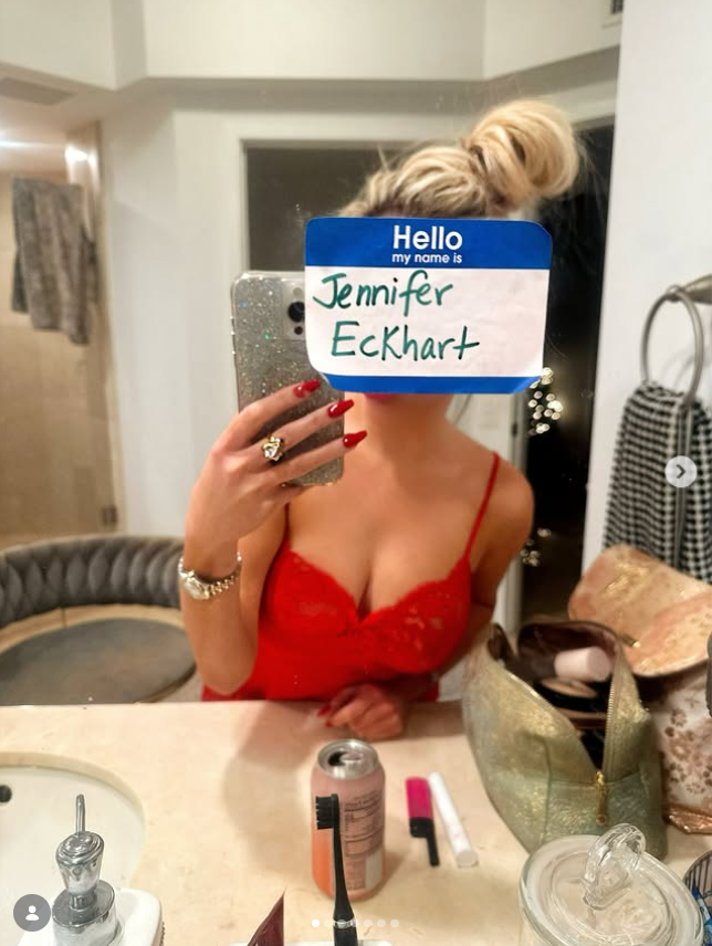 Jennifer Eckhart poses for a mirror selfie in a red lace outfit, holding a handwritten name tag that reads “Jennifer Eckhart.” | Source: Instagram/jennifereckhart