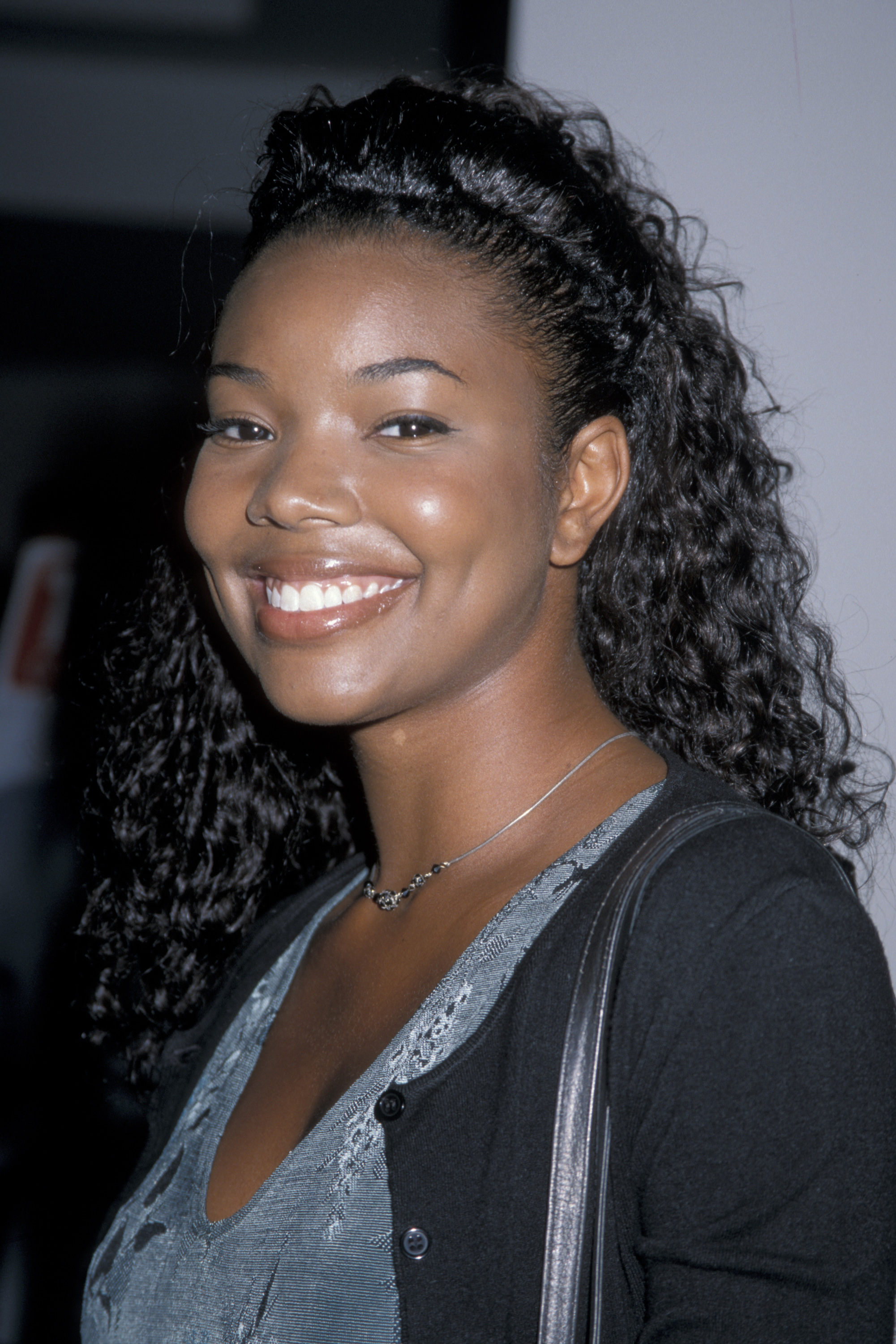 Gabrielle Union poses for a close-up portrait, smiling with her hair styled in soft curls, wearing a simple necklace and a dark cardigan over a patterned top. | Source: Getty Images