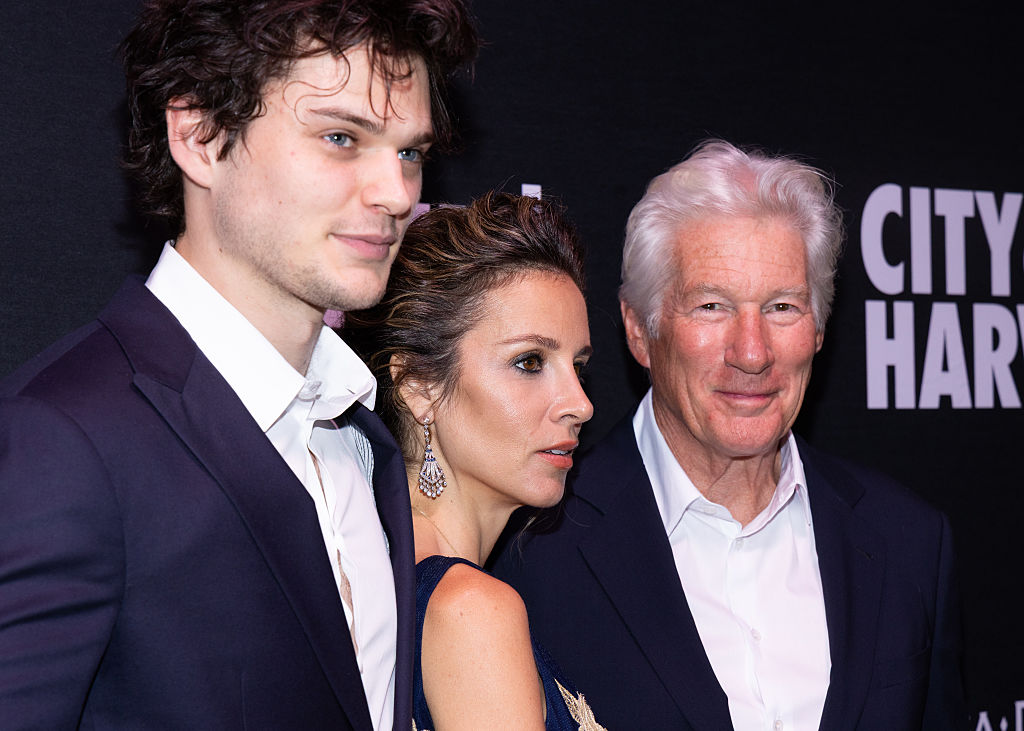 At the City Harvest Gala, Homer, Alejandra, and Richard Gere stand shoulder-to-shoulder, facing the cameras with composed elegance, each exuding quiet confidence and red carpet poise against the sleek backdrop.