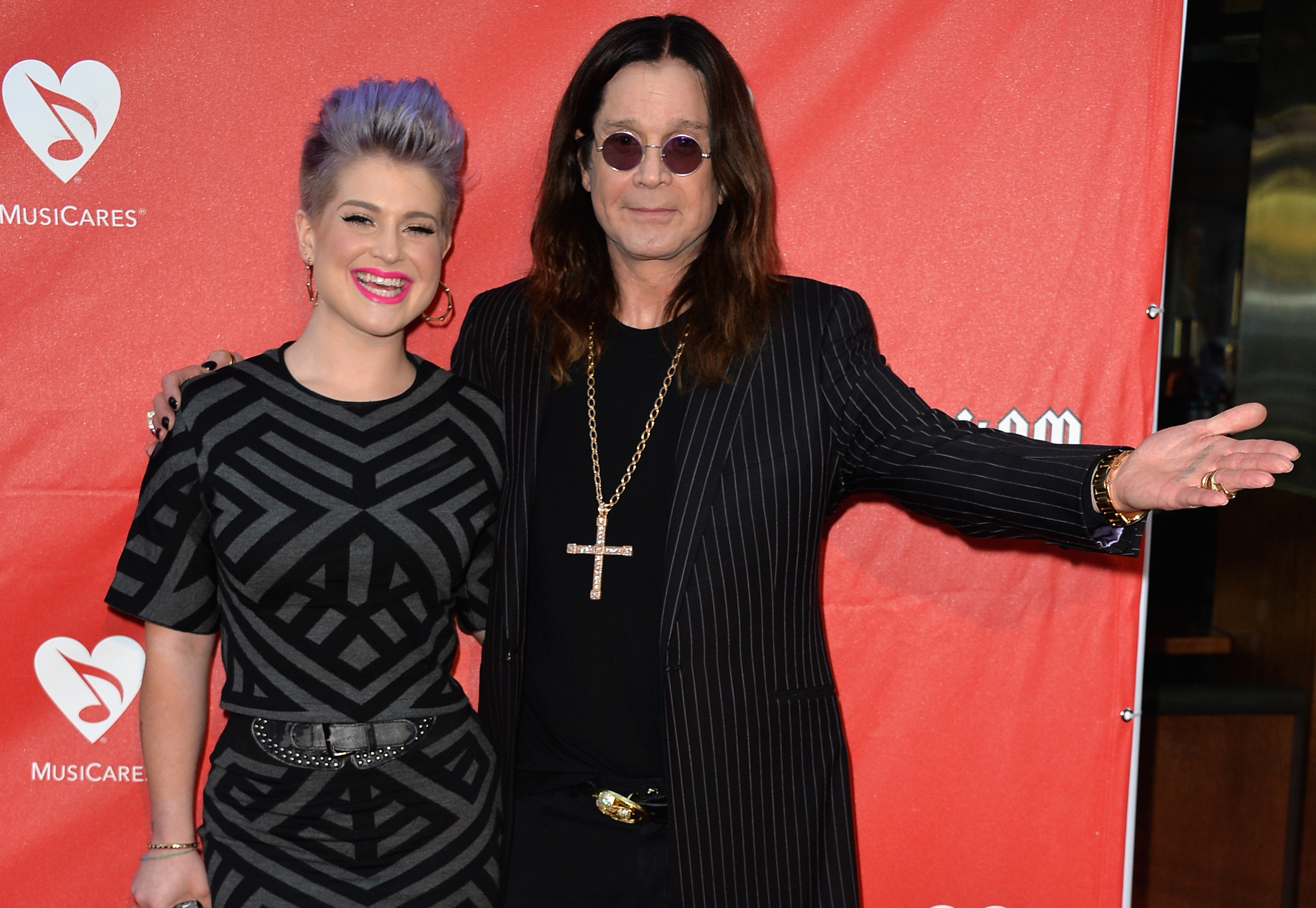 Kelly and Ozzy shared many public moments over the years. In one photo, they pose together at the 2014 MusiCares MAP Fund Benefit Concert in Los Angeles. Kelly smiles in a black patterned dress with short purple hair, while Ozzy stands beside her with one arm around her shoulders. | Source: Getty Images