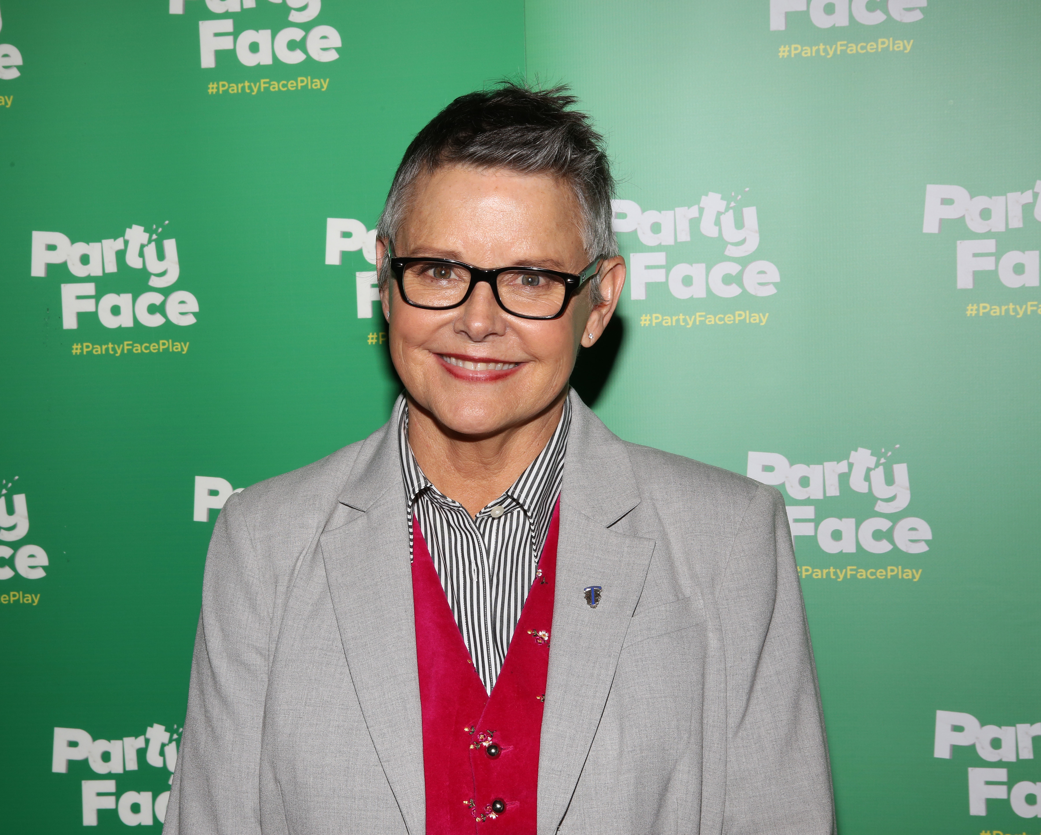 Amanda Bearse smiled warmly as she posed against the step-and-repeat backdrop at the opening night celebration of "Party Face" on January 22, 2018, held at Robert 2 Restaurant in New York City. The actress and director wore a tailored light grey blazer over a vibrant pink velvet vest, layered with a black-and-white vertically striped button-down shirt and finished with dark rectangular-framed glasses and her signature cropped pixie cut. | Source: Getty Images