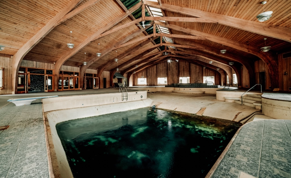 A neglected indoor swimming pool occupies the center of an enormous vaulted room inside Mike Tyson's former mansion, surrounded by tiled walkways and curved wooden beams overhead. Once part of the boxer's extensive collection of amenities, the deteriorating pool later became central to the property's transformation, with the church planning its main sanctuary within the approximately 10,000-square-foot space around it. | Source: Facebook/Johnny Joo