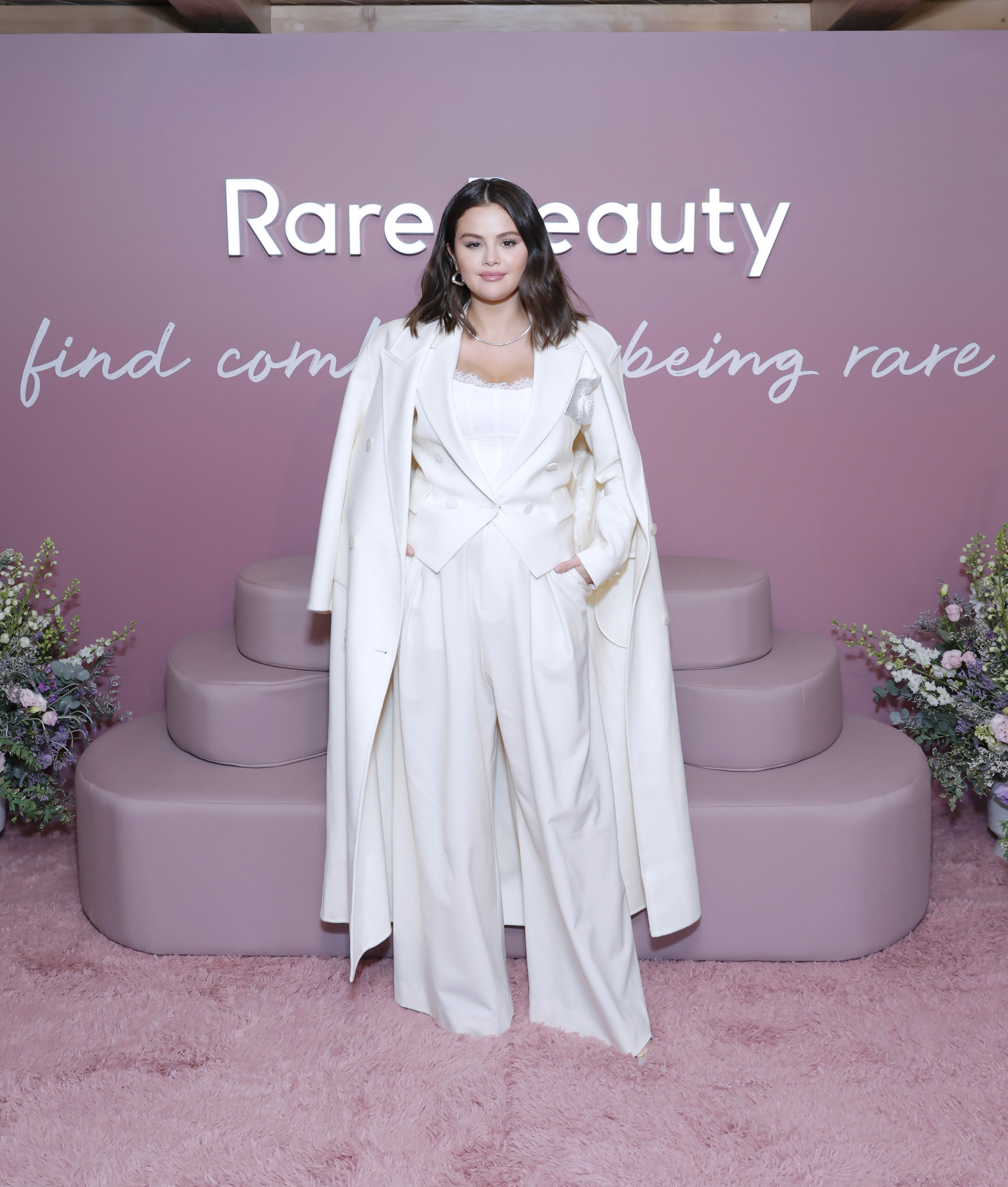 Selena Gomez celebrates the launch of Rare Beauty’s Find Comfort Body Collection in Beverly Hills, California. She exudes sophistication in a white palazzo pants, styled with a cropped coat layered under a long trench. With her hands tucked in her pockets, she strikes a poised, executive look that reflects her businesswoman edge.