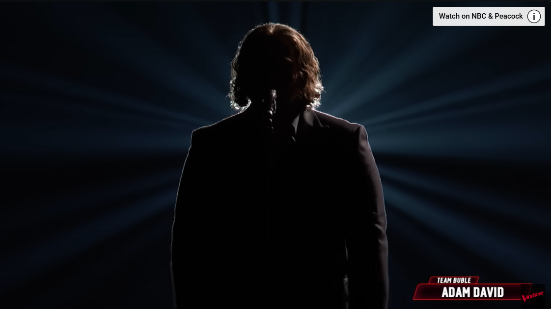 Adam David opens his finale performance in silhouette, standing center stage as beams of light radiate behind him | Source: YouTube/nbcthevoice