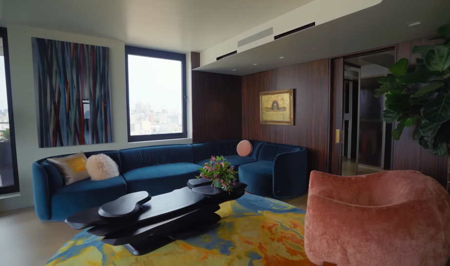 Sherman's jewel-tone palette gives the main living room an energy that feels miles away from a conventional beige celebrity apartment. Deep blue, dusty rose and a richly colored rug make the space sophisticated without taking itself too seriously. | Source: YouTube/Architectural Digest