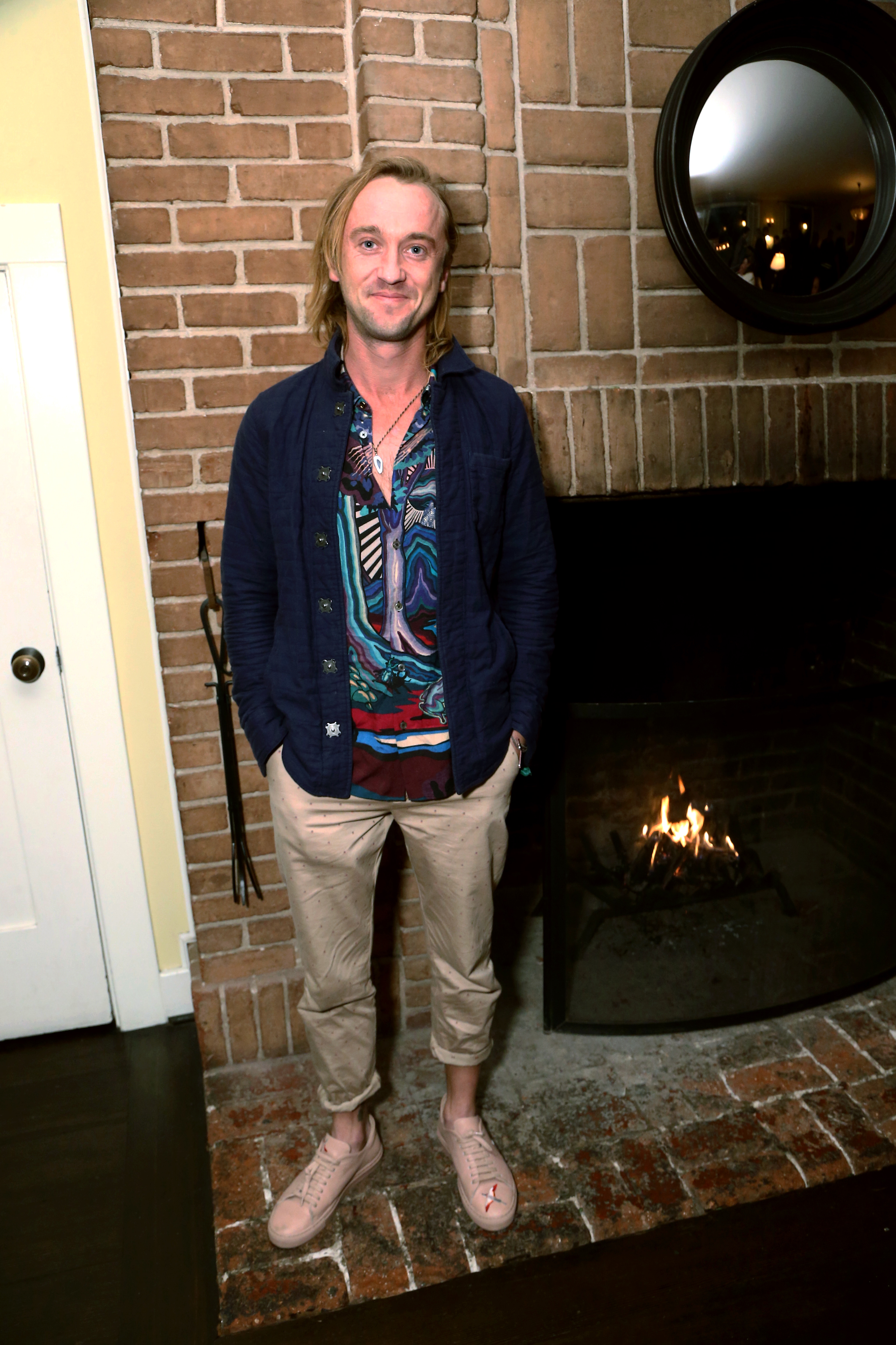 Tom Felton stands by a glowing fireplace, his vibrant patterned shirt adding a burst of color to the cozy setting. With a relaxed smile and hands tucked into his pockets, he exudes an effortlessly bohemian charm. At the Celebration of YouTube Originals, he blends warmth and style as naturally as the flames behind him.