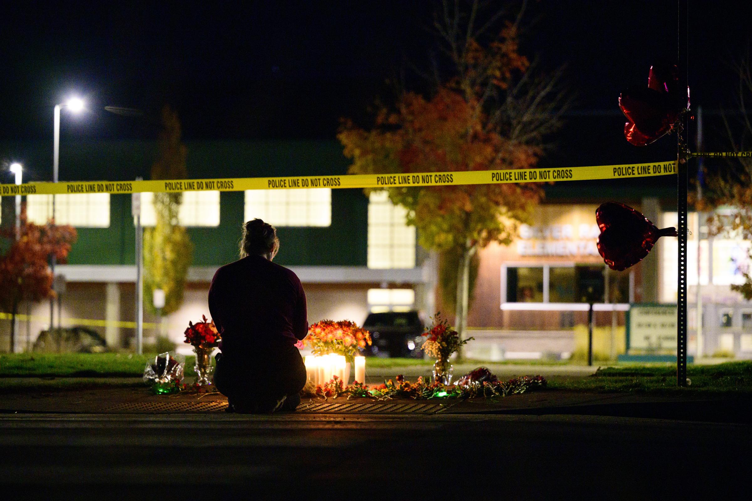 A lone mourner kneels before flowers and candles outside Silver Rail Elementary School as police tape surrounds the campus. | Source: Getty Images