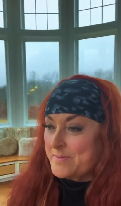 Wynonna appears in front of tall windows that wrap around a rounded section of the room. A cushioned window seat runs beneath the glass, while the view outside offers another perspective on the home's surroundings. | Source: Instagram/wynonnajudd