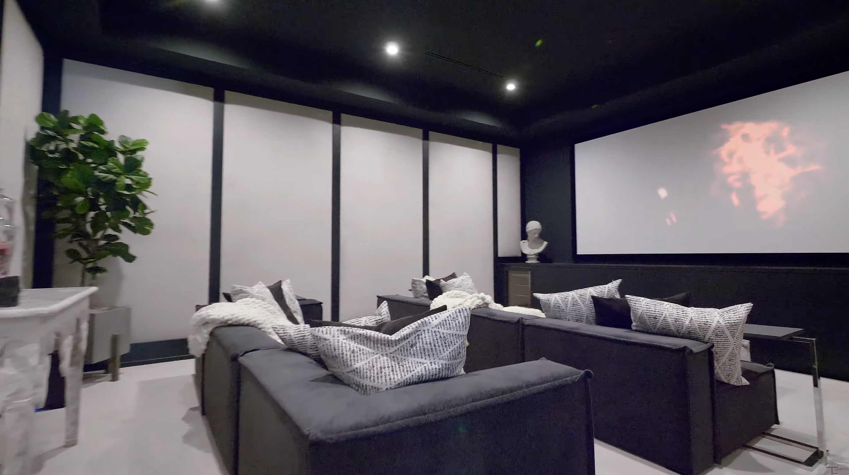 Dark walls and ceilings give the screening room a more enclosed atmosphere than the rest of the house. Several rows of deep sofas face a large screen at the front. | Source: Youtube/Tomer.Fridman