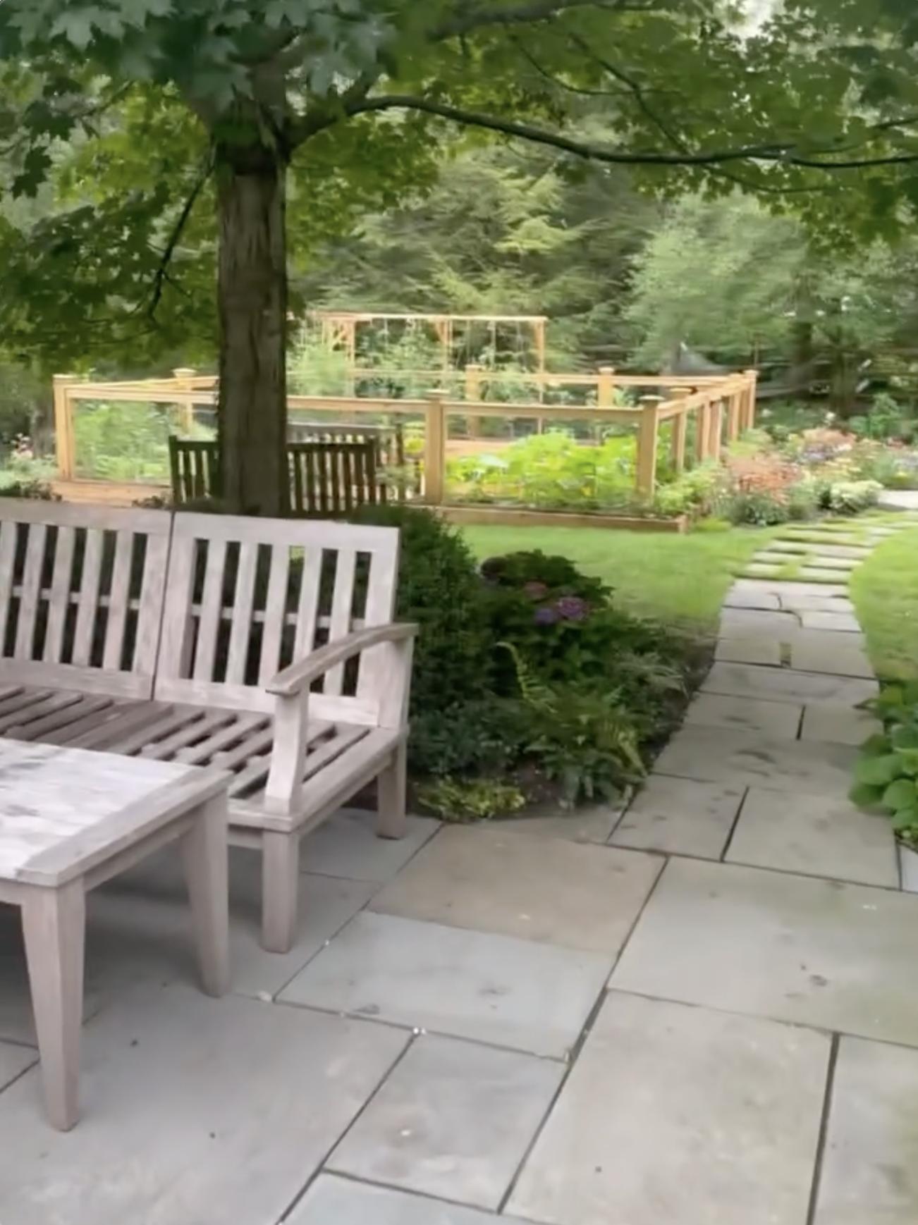 A winding pathway leads past outdoor seating and landscaped gardens toward a fenced planting area on the grounds of the family's residence. | Source: Instagram/alejandragere