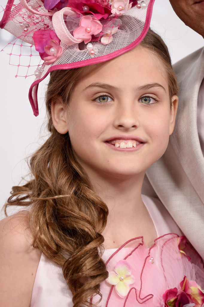 A structural, fuchsia-trimmed headpiece woven with fine netting and pearl-centered blossoms sat perched above glossy curls, which swept neatly over one shoulder as 10-year-old Dannielynn Birkhead arrived at Churchill Downs on May 6, 2017. Outfitted in a soft rose dress accented by textured petal motifs, she met the cameras at the 143rd Kentucky Derby with an easy, toothy grin and an effortless familiarity with the storied springtime tradition.