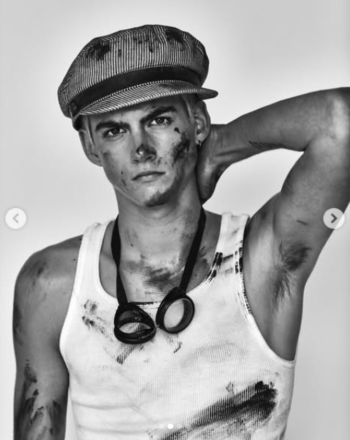 In a black-and-white modeling throwback shared to his account in 2024, Presley Gerber channeled a gritty industrial aesthetic, posing with one hand behind his neck while sporting a pinstriped newsboy cap, protective goggles hanging around his neck, and soot-smudged skin in a white ribbed tank top. | Source: Instagram/presleygerber
