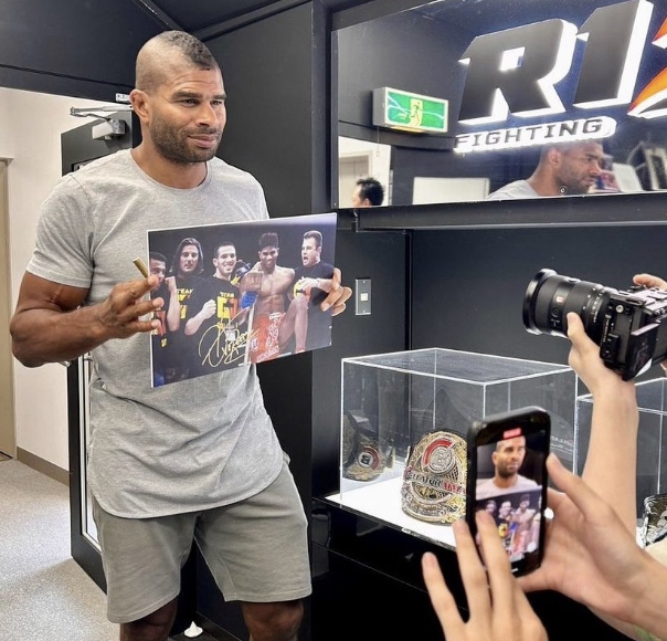 Holding the signed photograph for cameras, Alistair Overeem provided another clear look at the slimmer body that surprised followers accustomed to his imposing fighting-era appearance. His reduced size was especially noticeable through his arms and torso, creating a sharp visual contrast with the muscular heavyweight seen at UFC weigh-ins years earlier. Overeem later explained that his appetite and eating habits had changed after he began detoxing and following a supplement regimen recommended by his nutritionist.. | Source: X/COMBAT SPORTS TODAY