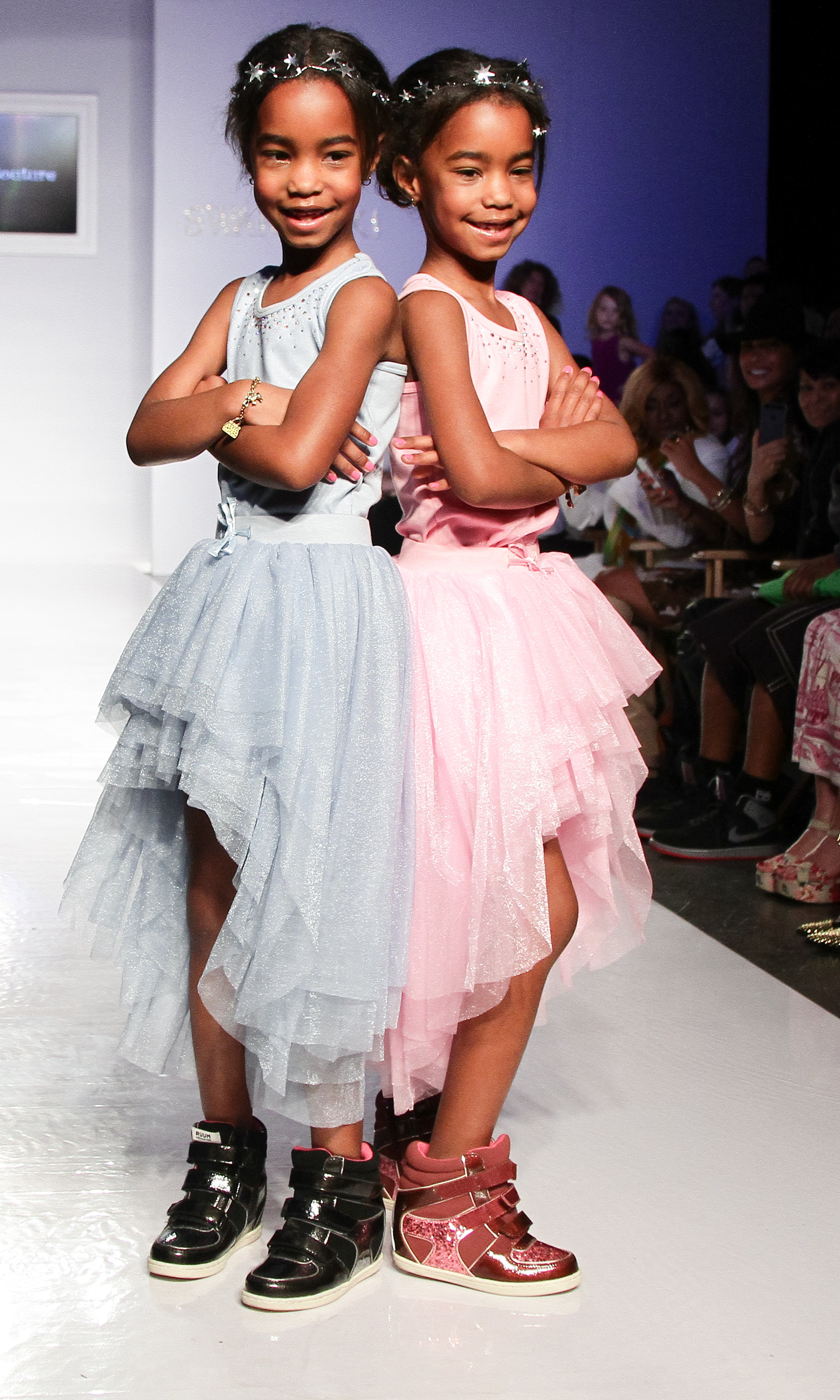Jessie James and D’Lila Star Combs pose back-to-back on the runway in sparkling pastel dresses and matching headbands, bringing playful confidence to the fashion week spotlight.