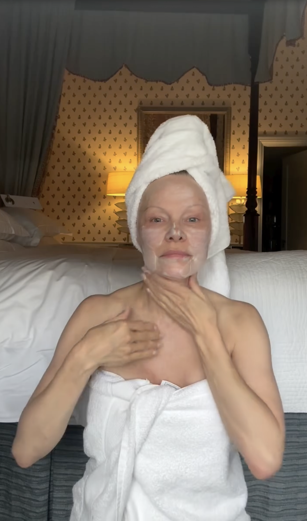Pamela Anderson applies moisturizer to her neck and chest while wrapped in white bath towels with a matching towel turban after a morning routine. Radiating natural self-acceptance, she celebrated the anniversary of her holistic skincare line Sonsie Skin, pairing the bare-faced bedroom video with a thoughtful reflection: "Good morning world… 🤍 Today is a blessing—as we mark another @sonsieskin birthday. The universe is granting wishes… what are yours? Mine is to be even more grateful, playful… and wise. ✨ Love, P". | Source: Instagram/pamelaanderson