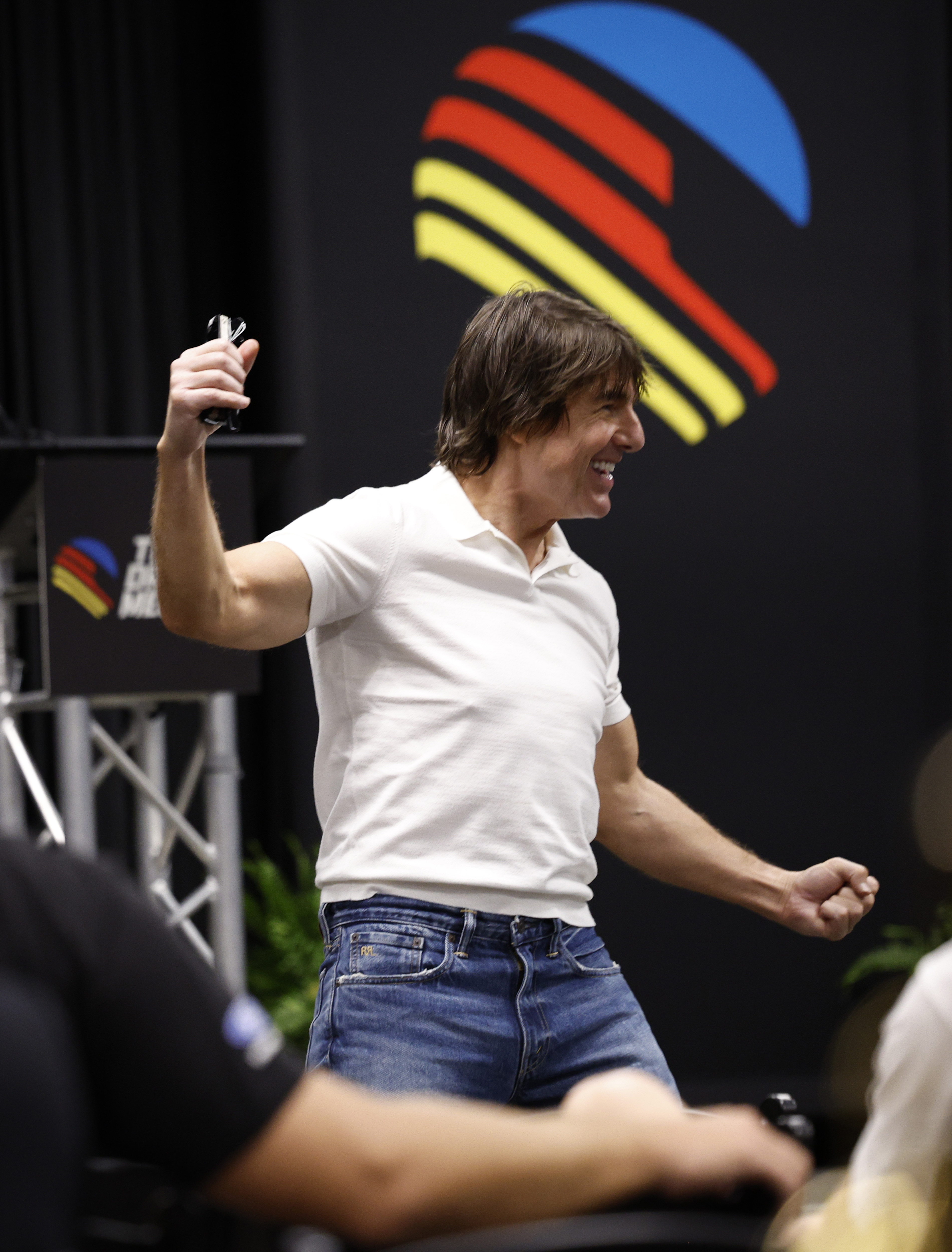 Cruise smiles and raises one arm while speaking to guests inside the Daytona gathering. The photo captures him without the dark sunglasses he wore outside, offering a clearer view of his face and hairstyle. | Source: Getty Images
