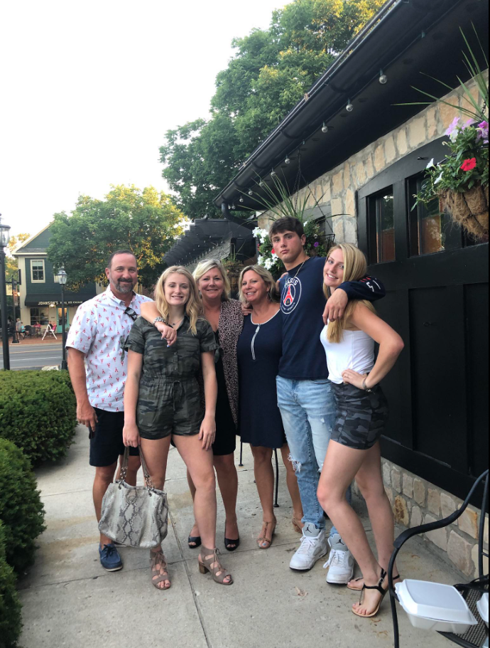 Outside along a sidewalk, Jack Pugh stands with a group, arms draped casually — an easy, sunlit snapshot of connection and shared time. | Source: Facebook/KennaLynMcClelland