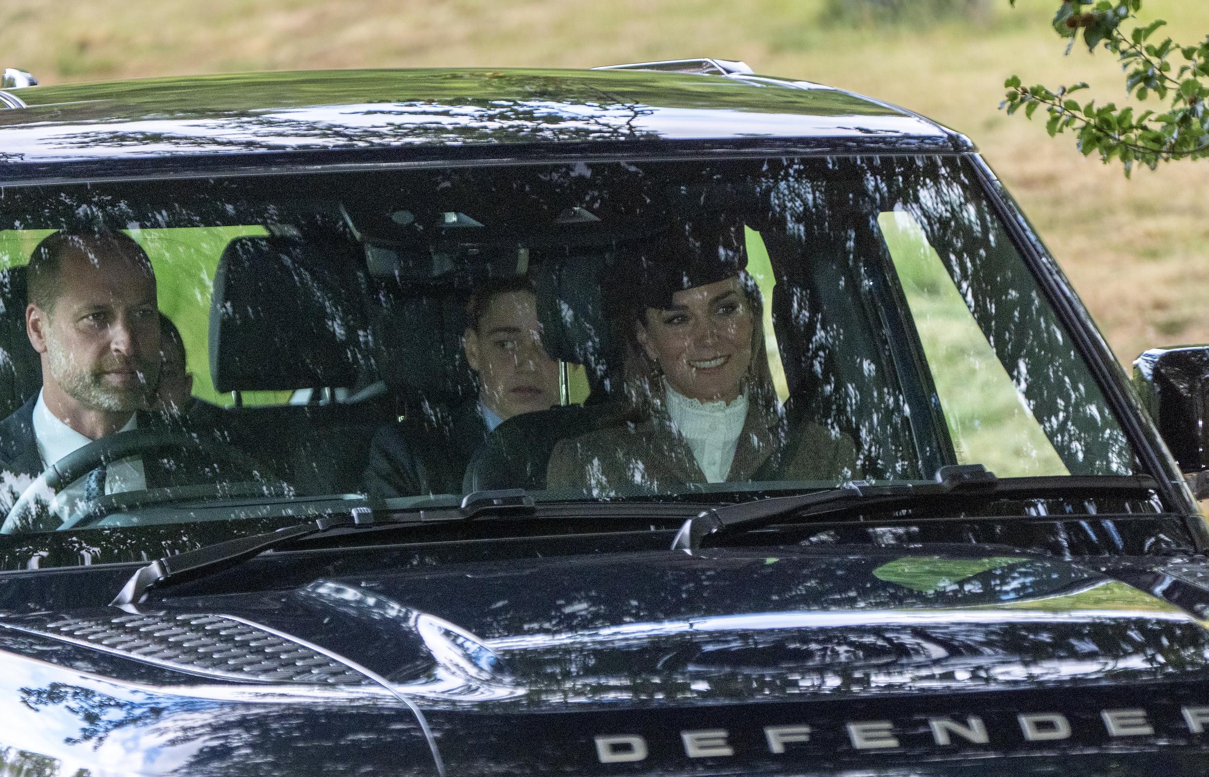A wide view through the windshield shows Prince William at the wheel and Catherine, Princess of Wales, in the passenger seat, with Prince George visible in the front. | Source: Getty Images