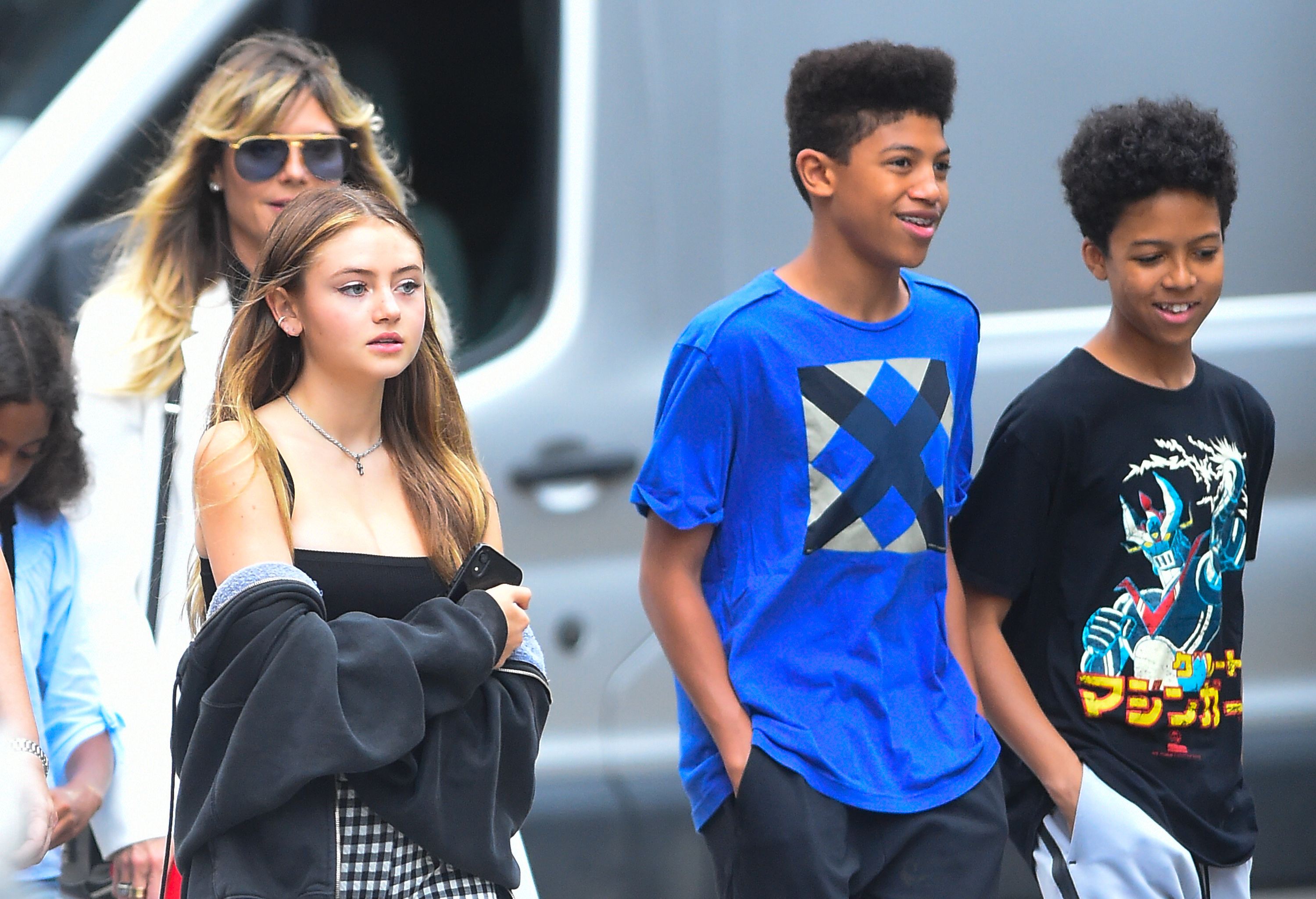 Johan and Henry Samuel walk side by side, looking cheerful and stylish—one in a vibrant blue geometric tee and the other in a bold black anime graphic shirt. Their relaxed demeanor and casual outfits highlight a carefree outing moment with family in the city.