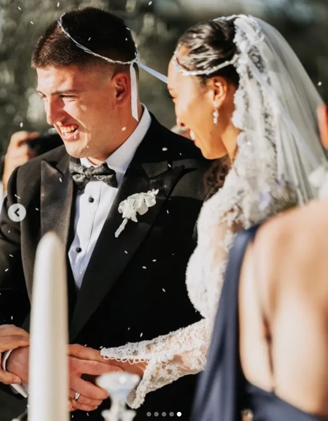 George Karlaftis and Kaia Harris smile as they walk together following their wedding ceremony, surrounded by falling white confetti. | Source: Instagram/georgekarlaftis