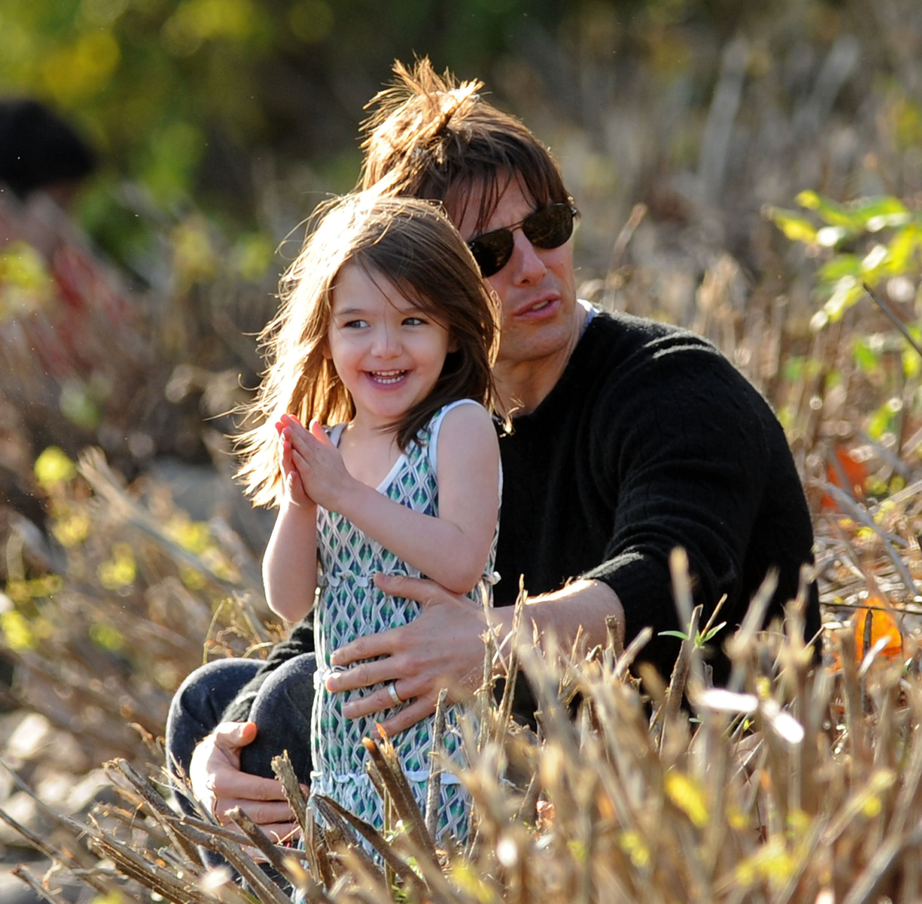 In this heartwarming scene, a toddler-aged Suri Cruise shares a quiet moment with her father, Tom Cruise, out in the open fields. The two appear relaxed and connected, surrounded by nature and free from the usual flash of cameras.