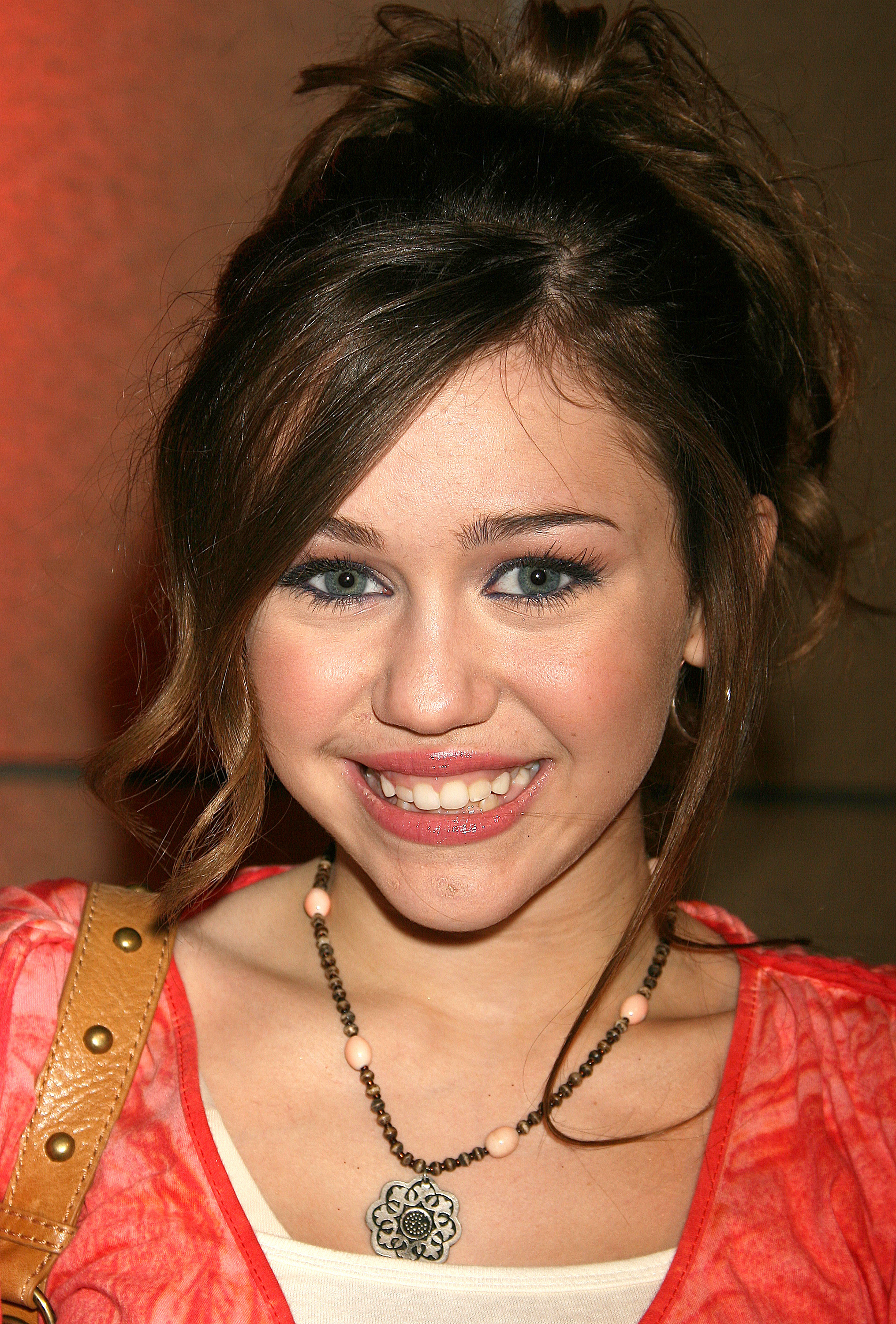 Miley Cyrus posed with her hair swept into an updo, wearing a coral top over a white shirt and a statement necklace during her early years in the spotlight. Her youthful appearance recalls the period when she was balancing her everyday identity with the glamorous image of her Disney character. | Source: Getty Images