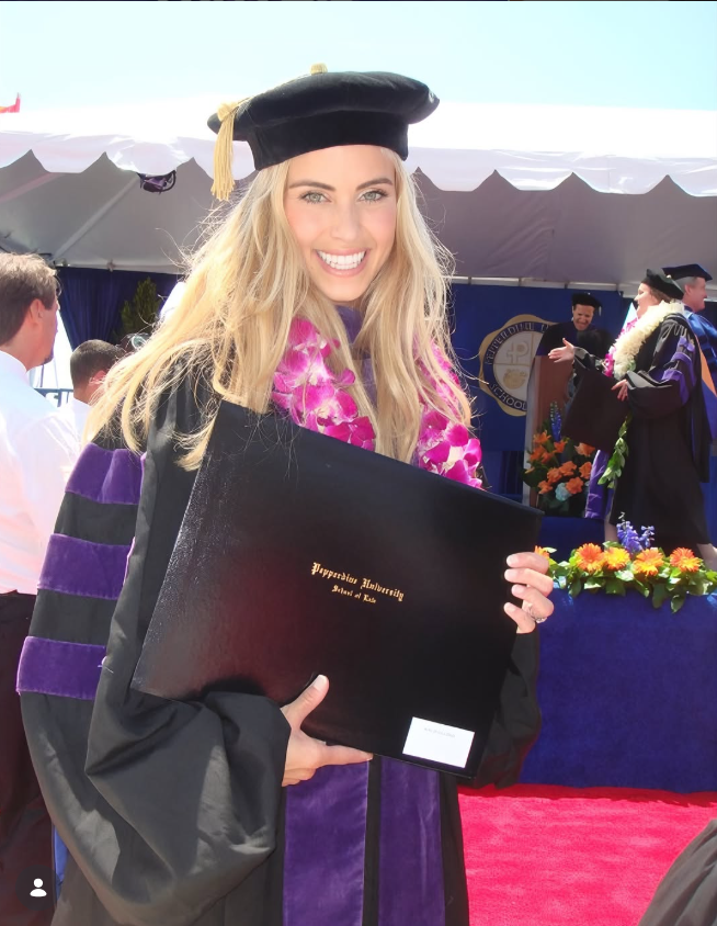 Katie Zacharia celebrates her graduation from Pepperdine Caruso School of Law in a black academic gown, purple-trimmed regalia, and a doctoral-style cap, holding her diploma folder. Her time at Pepperdine helped lay the foundation for a career that would later take her from legal studies to political communications and the White House. | Source: Instagram/katiezacharia