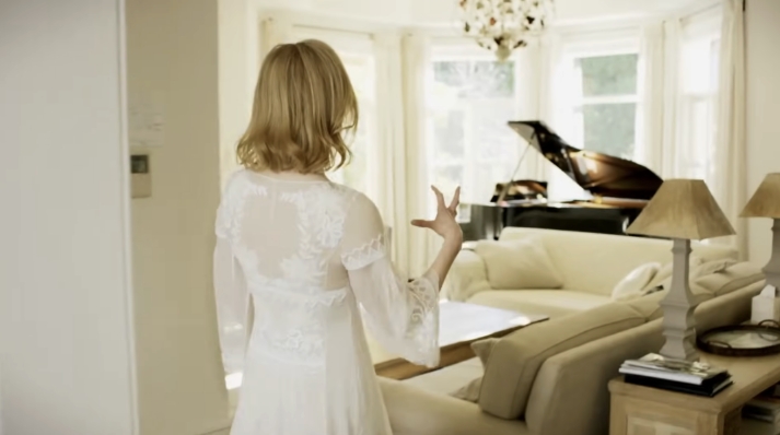 A bright and airy sitting room opens up with cream furnishings, soft natural light, and a striking black grand piano positioned in the bay window — a blend of elegance and comfort. From a video dated July 20, 2015. | Source: YouTube/Vogue