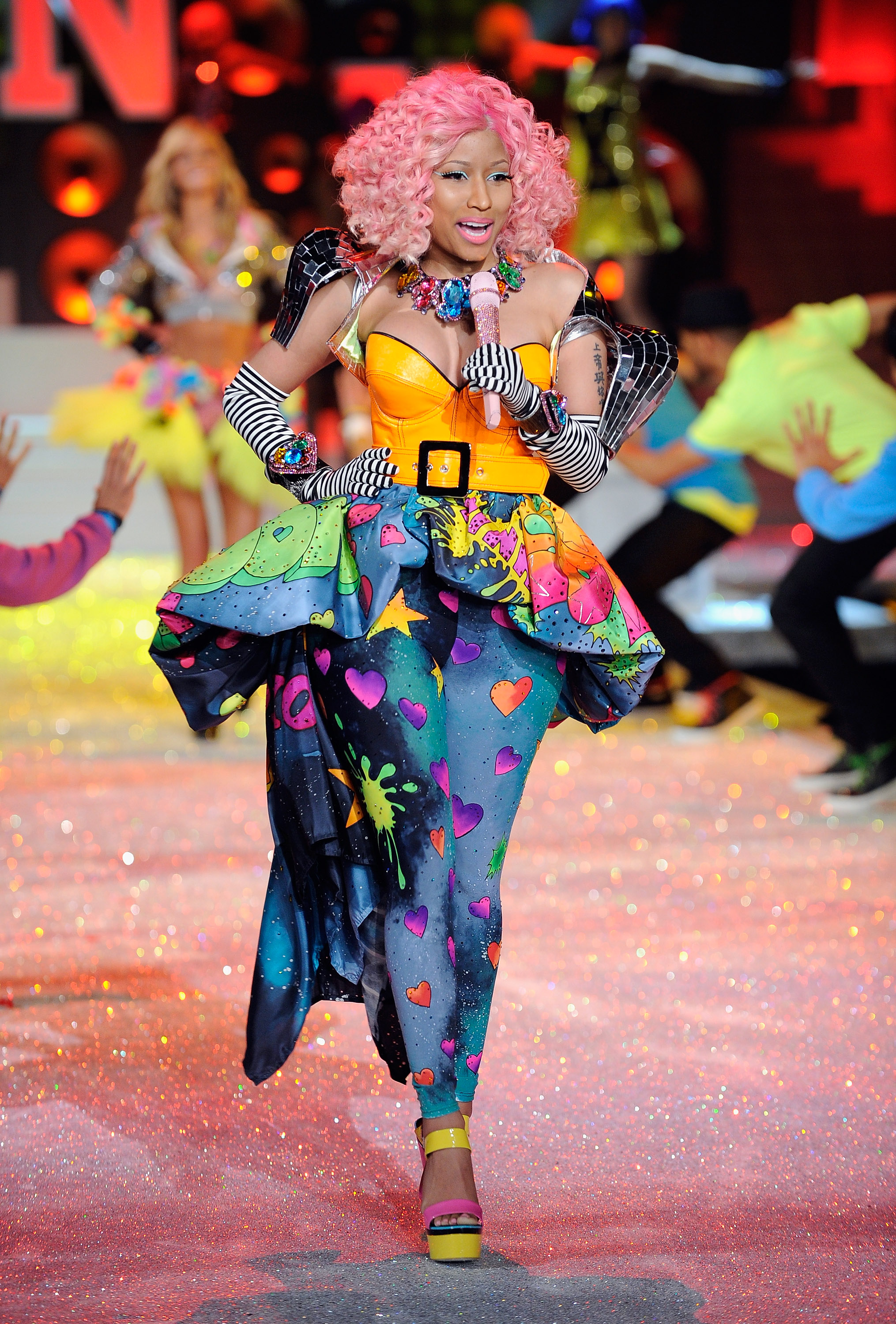 Nicki Minaj performs her hit "Super Bass" at the 2011 Victoria's Secret Fashion Show in New York, wearing a bright orange corset, a colorful heart-patterned outfit, and a curly pink wig. Her performance was part of the show's Club Pink segment. | Source: Getty Images