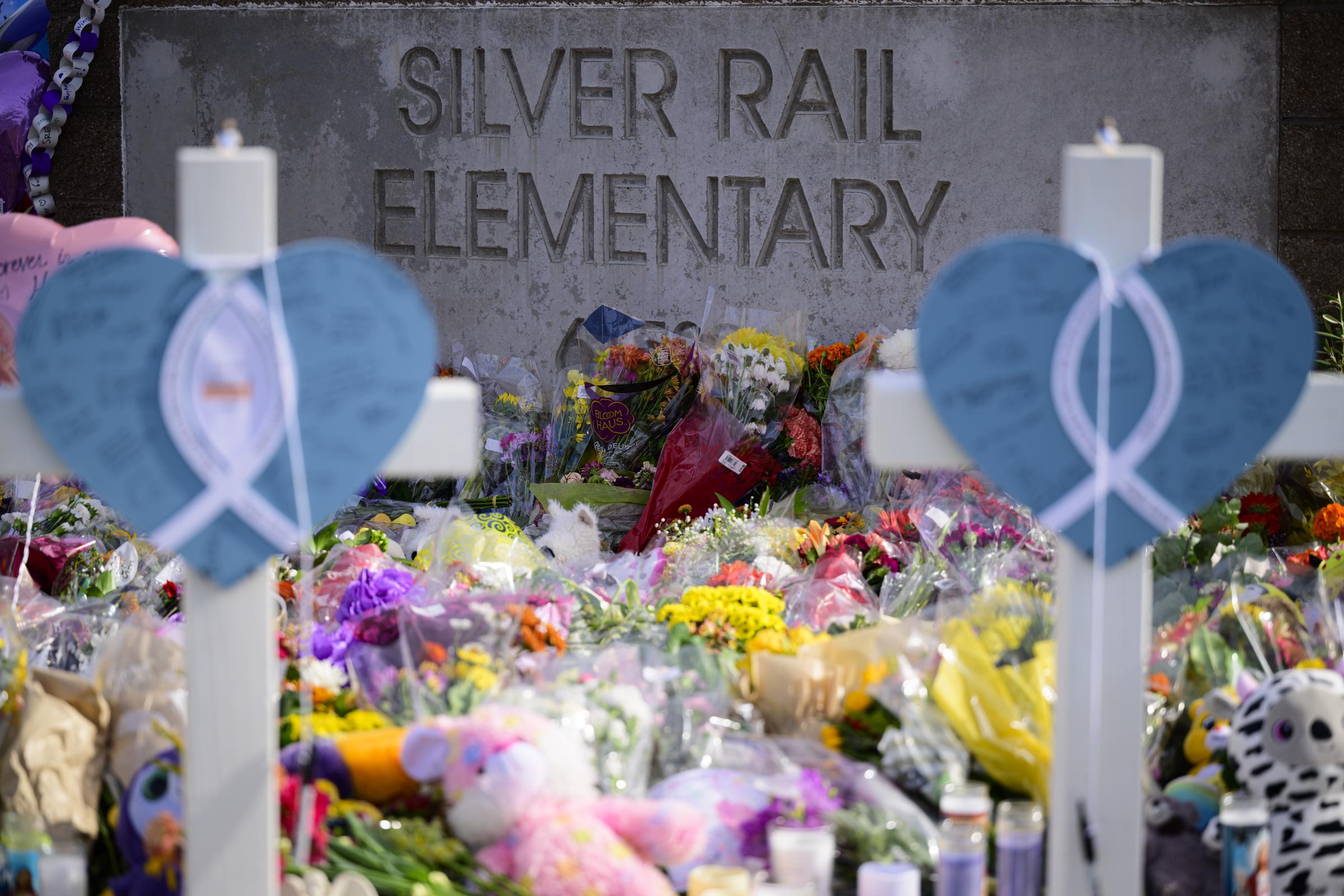 Blue hearts with white ribbons, flowers, and children's toys filled the memorial outside Silver Rail Elementary, honoring the three young boys and 25-year-old teacher who lost their lives. | Source: Getty Images
